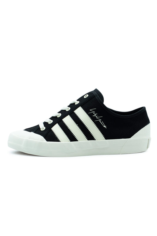 Lateral side profile view of the Adidas Y-3 Nisi Lo sneaker in Black / Off White, featuring a black canvas upper with serrated off-white leather 3-Stripes, an off-white printed Yohji Yamamoto signature script, off-white laces, and a vulcanized rubber sole with an elevated toe cap.