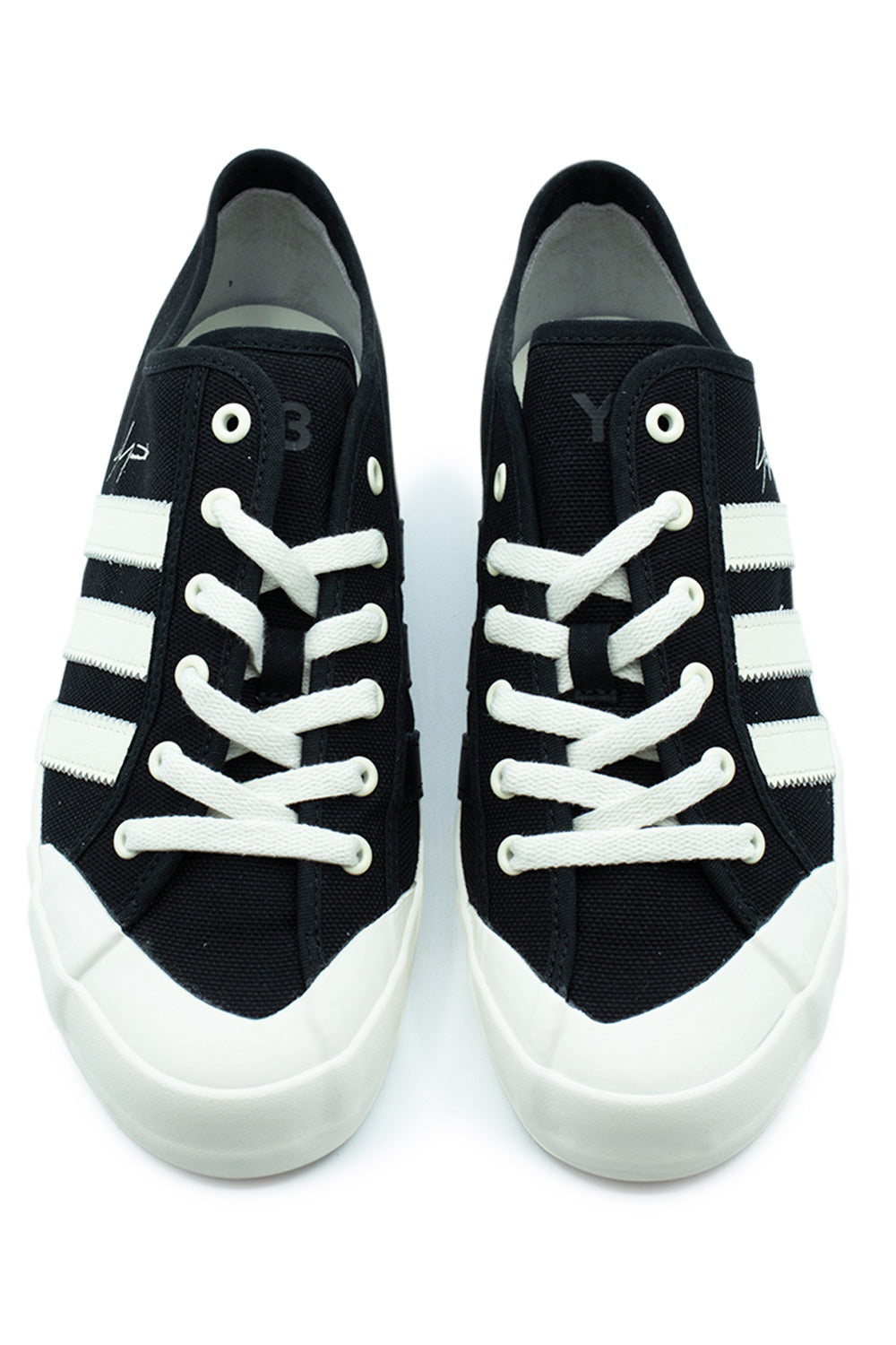 Top-down perspective of a pair of low-top Adidas Y-3 Nisi Lo canvas sneakers, showcasing the radical asymmetrical lacing system, off-white flat cotton laces, white metal eyelets, off-white rubber toe bumper, and subtle black Y-3 branding printed on the canvas tongues.