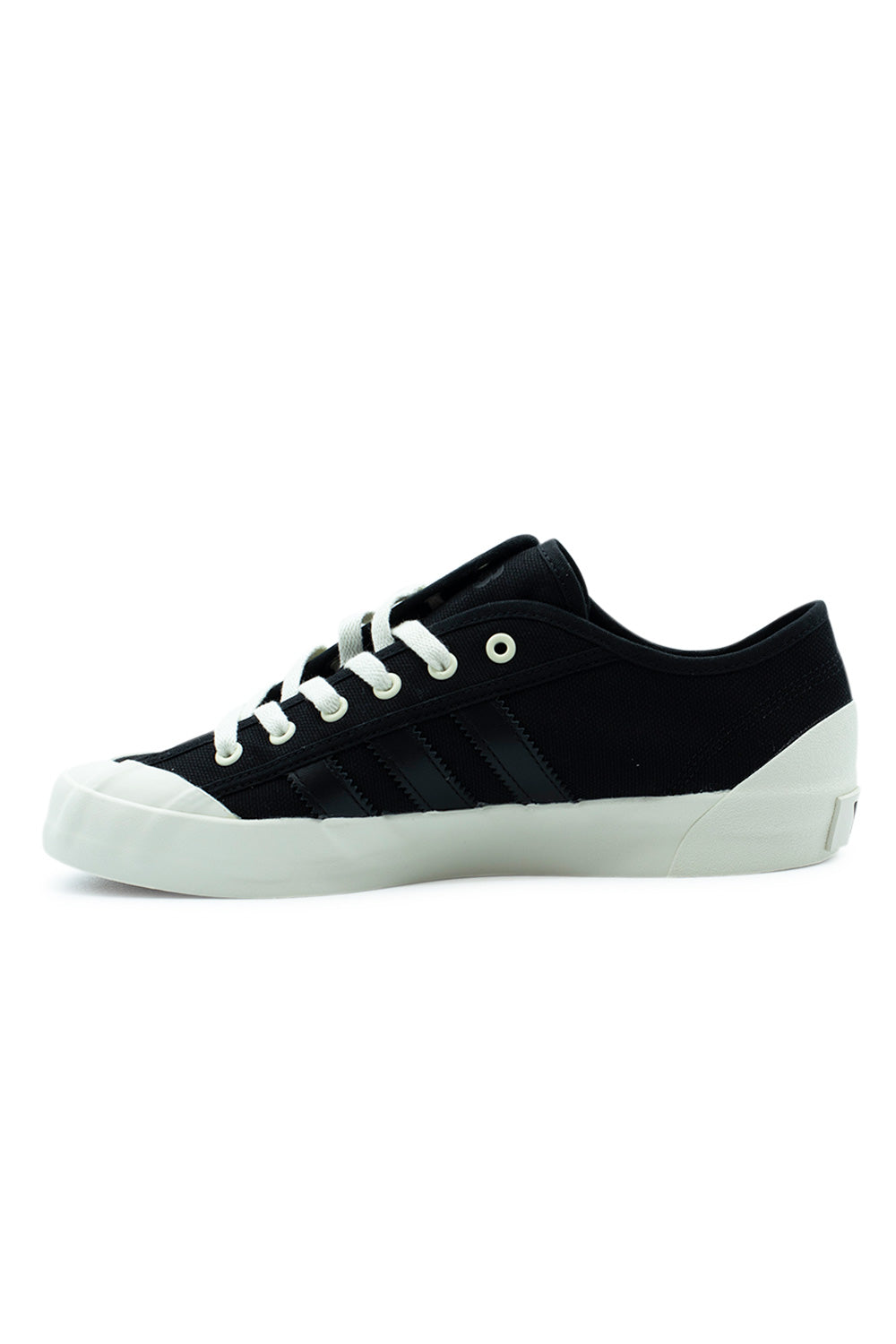 Medial side profile view of the Adidas Y-3 Nisi Lo shoe, highlighting the tonal shadow aesthetic with black leather 3-Stripes on black canvas, off-white vulcanized rubber sidewall, and white toe cap extension without the script signature.