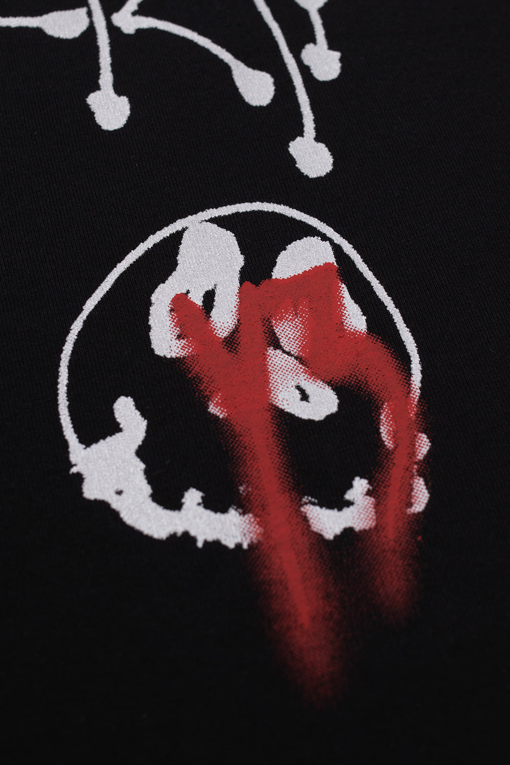 Close-up macro detail of the circular white airbrushed smiley skull graphic accented with bright red dripping spray paint strokes on the chest of the black Adidas Y-3 X Chito shirt.