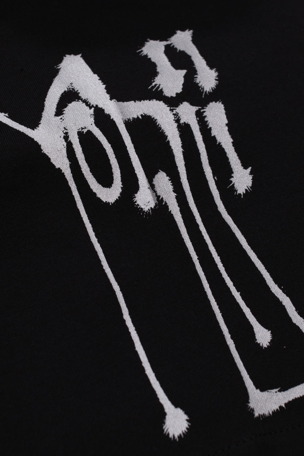 Macro detail view of the white dripping Yohji tag artwork screen-printed along the left sleeve of the black cotton Adidas Y-3 X Chito City Graphic Short Sleeve Tee.