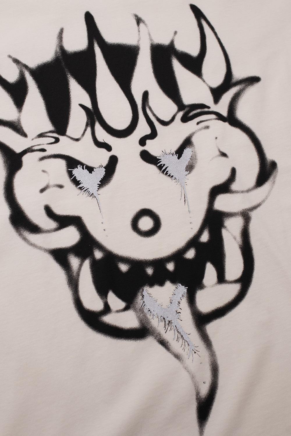 Close-up of the black airbrushed horned creature face graphic on the chalk white Adidas Y-3 x Chito capsule tee, highlighting glittery silver metallic highlights on the eyes and tongue.