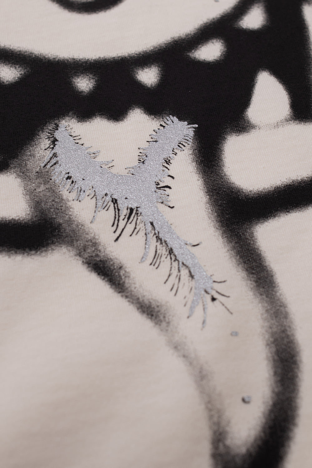 Macro detail shot of the glittery silver metallic paint finish on the protruding tongue and teeth of the monster artwork printed on the chalk white Adidas Y-3 x Chito KU2249 T-shirt.