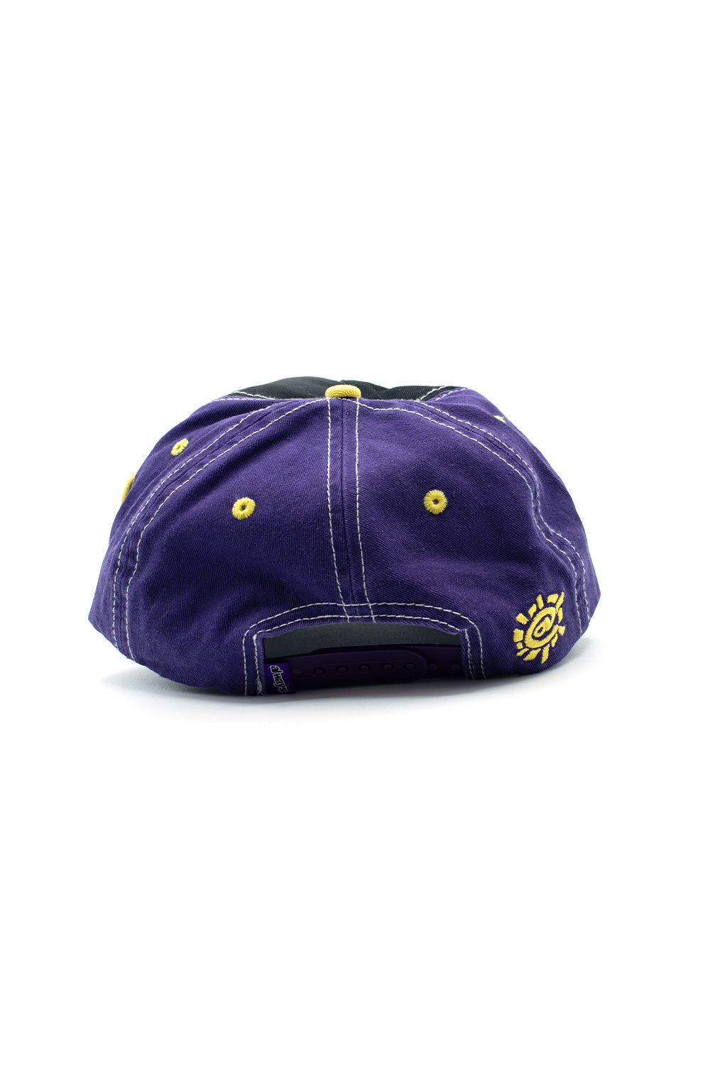Rear perspective shot of the purple cotton crown of the Always Human Logo 5 Panel Cap, displaying white contrast seam stitching, yellow embroidered eyelets, an adjustable purple plastic snap closure with a purple brand flag tag, and a bright yellow embroidered Always @sun spiral logo on the lower right panel.