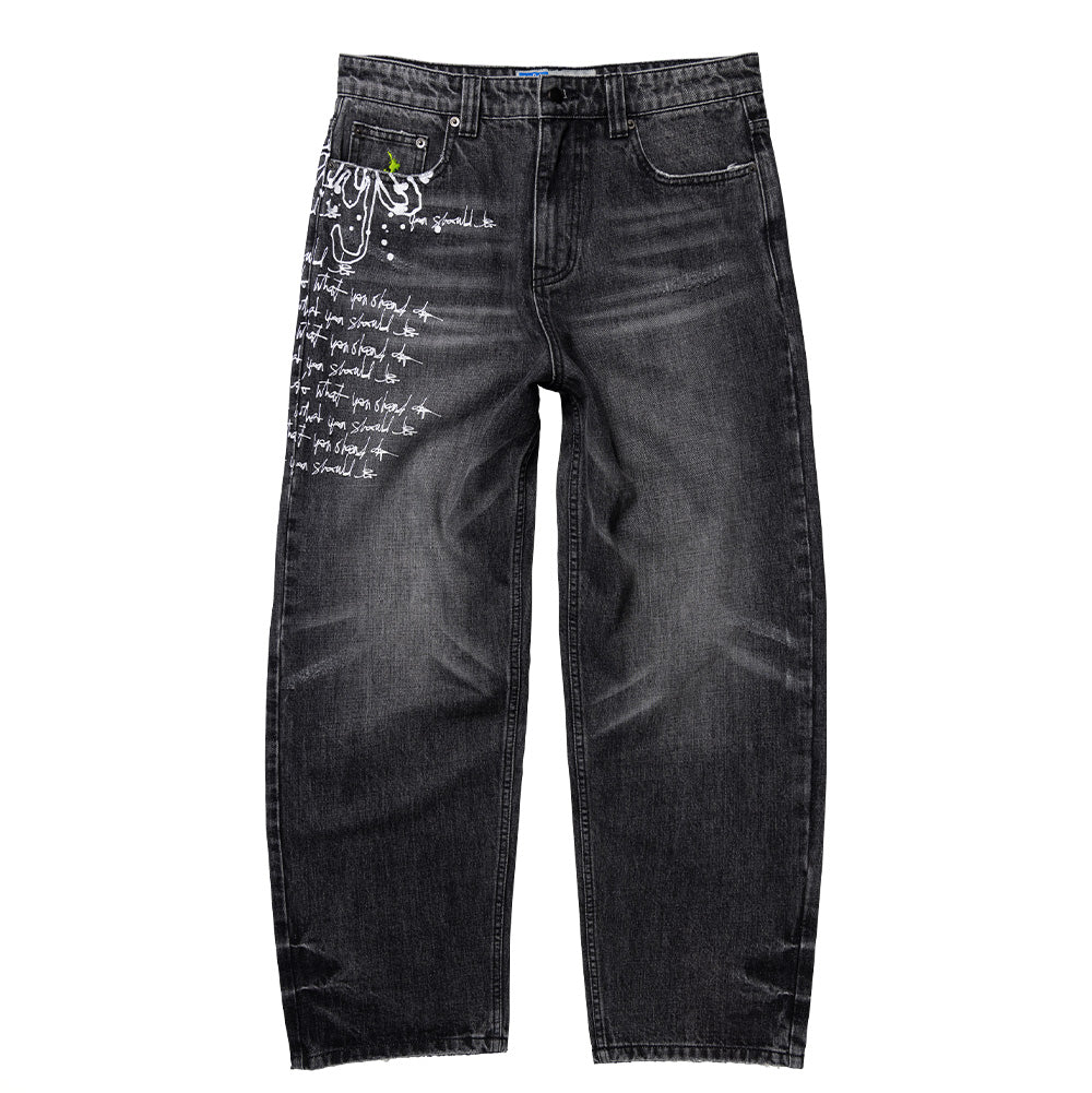 Front flat lay view of the Always Do What You Should Do Waza Jeans in washed black denim, showcasing a relaxed fit with slightly tapered legs, classic five-pocket construction, washed charcoal grey fading across the thighs, custom metal rivets, and bold white graffiti-style paint drip lettering and repetitive handwritten script running down the entire right leg.