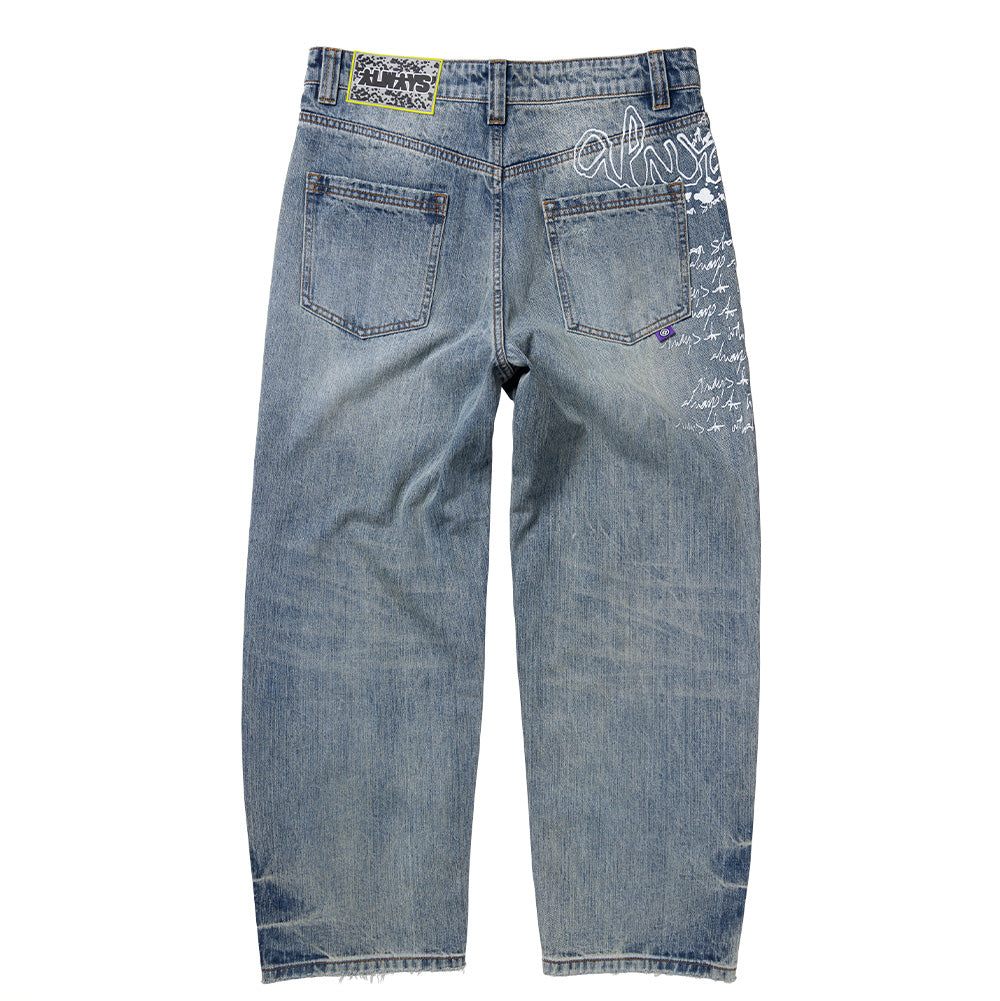 Back flat lay view of the Always Do What You Should Do Waza Jeans in washed light blue denim, featuring a yellow-bordered black textured jacron back patch on the waistband, dual rear patch pockets, a small purple logo flag tag, and a stylized white screen-printed graffiti graphic spanning the upper right hip down the side seam.