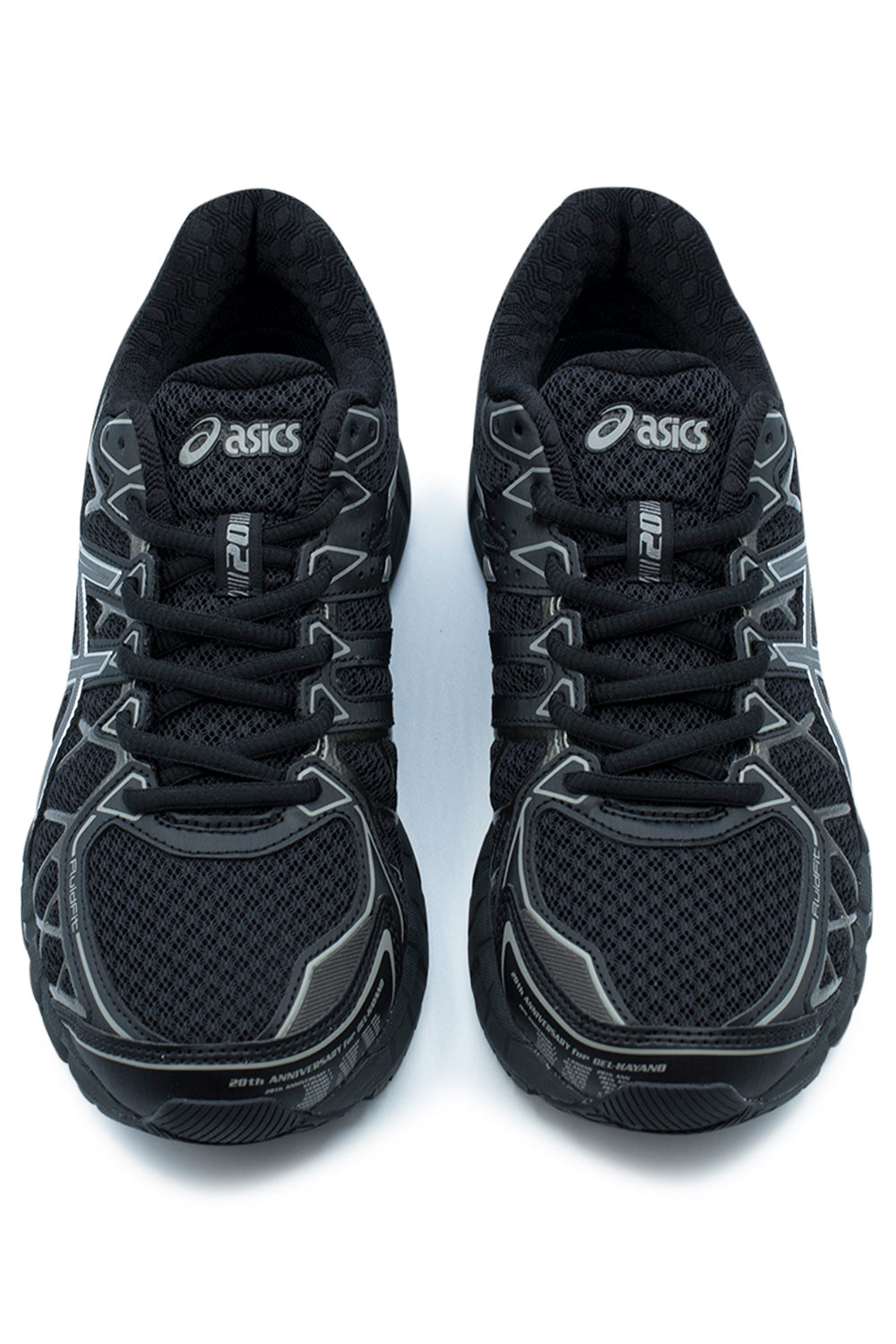 Top-down studio shot of a pair of black Asics Gel-Kayano 20 running shoes, highlighting the wide-mesh toe boxes, tonal black synthetic toe mudguards with "20th ANNIVERSARY for GEL-KAYANO" typographic details, black round laces laced through webbed eyelets, and padded mesh tongues with white Asics logo badges and "20" lace loops.