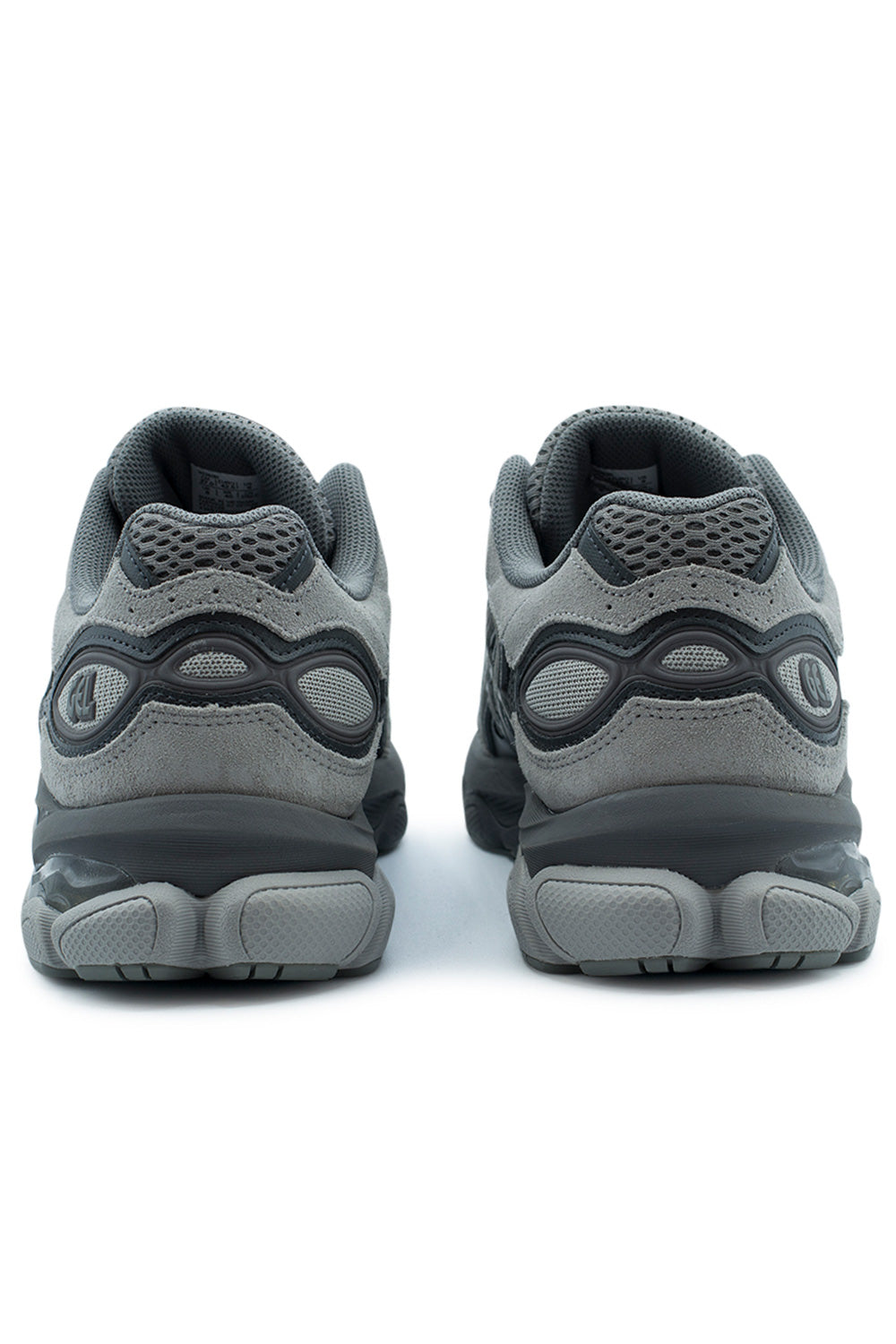 Rear perspective shot of the heels of the Asics Gel-NYC 2.0 shoes, displaying the layered grey suede heel counters, open-cell mesh collar pods, reflective oval cutouts framed by a dark grey molded TPU support cage with embossed "GEL" branding, and the textured AHAR rubber outsole wrap.