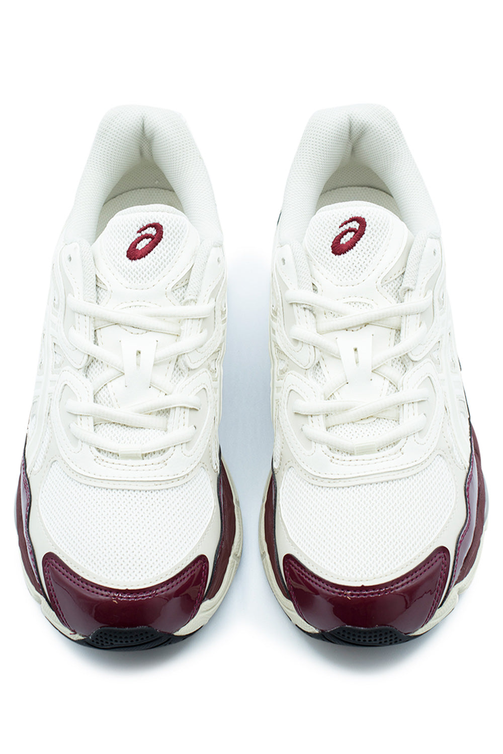 Top-down studio shot of a pair of Asics Gel-NYC shoes, displaying the cream open mesh toe box, high-gloss antique red patent leather toe caps, flat cream laces threaded through multi-layered eyestays, and mesh tongue tabs embroidered with burgundy Asics spiral logos