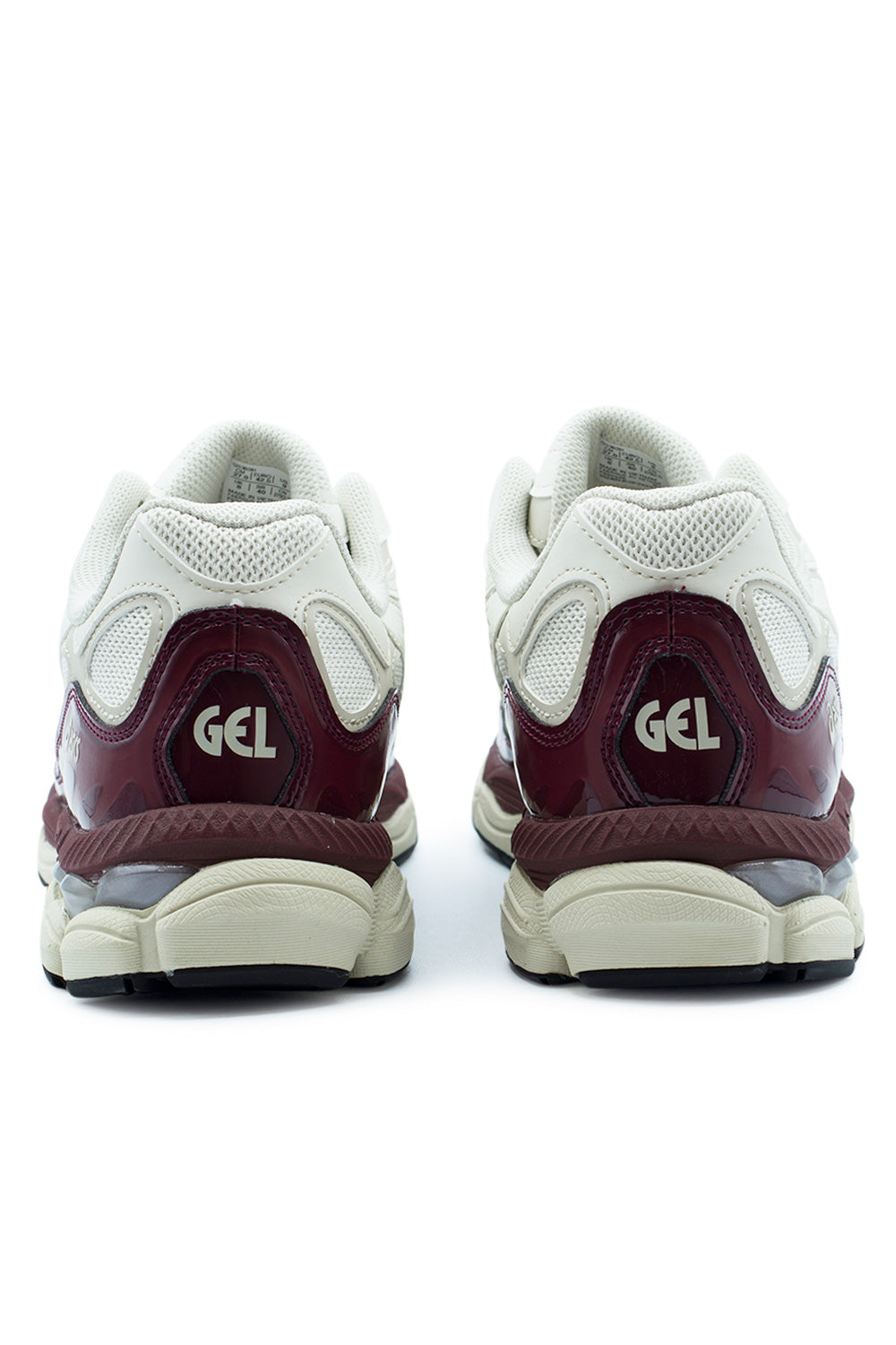 Rear perspective shot of the heels of the Asics Gel-NYC sneakers, showing the cream synthetic overlays, breathable mesh collar lining, segmented antique red patent leather counter cups embossed with silver "GEL" branding, and the cream rubber sole finish