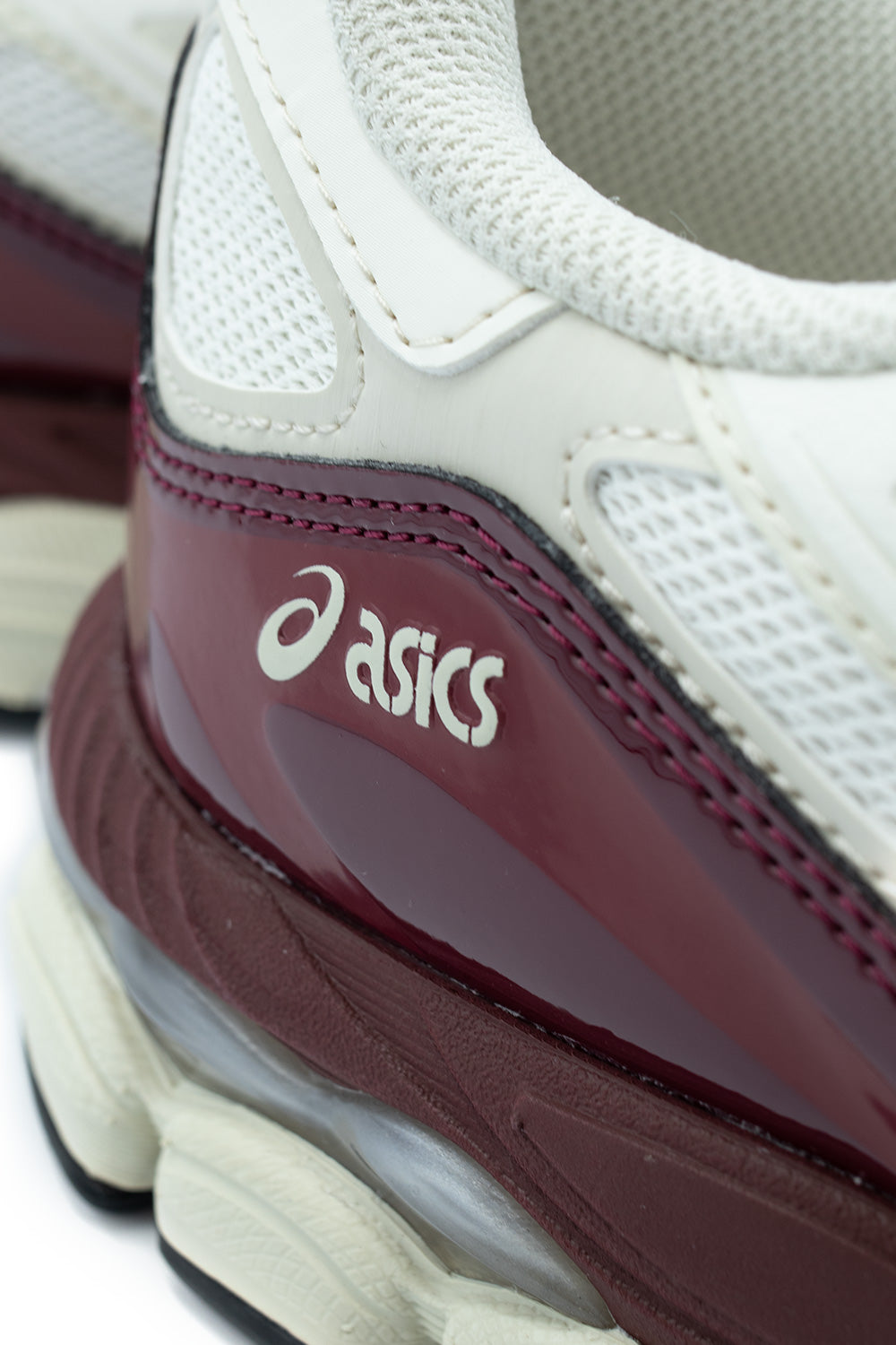 Macro close-up shot of the lateral rear quarter on the Asics Gel-NYC, highlighting the glossy antique red patent leather counter panel printed with silver "asics" typography, tonal stitching, and visible grey GEL cushioning pod in the heel