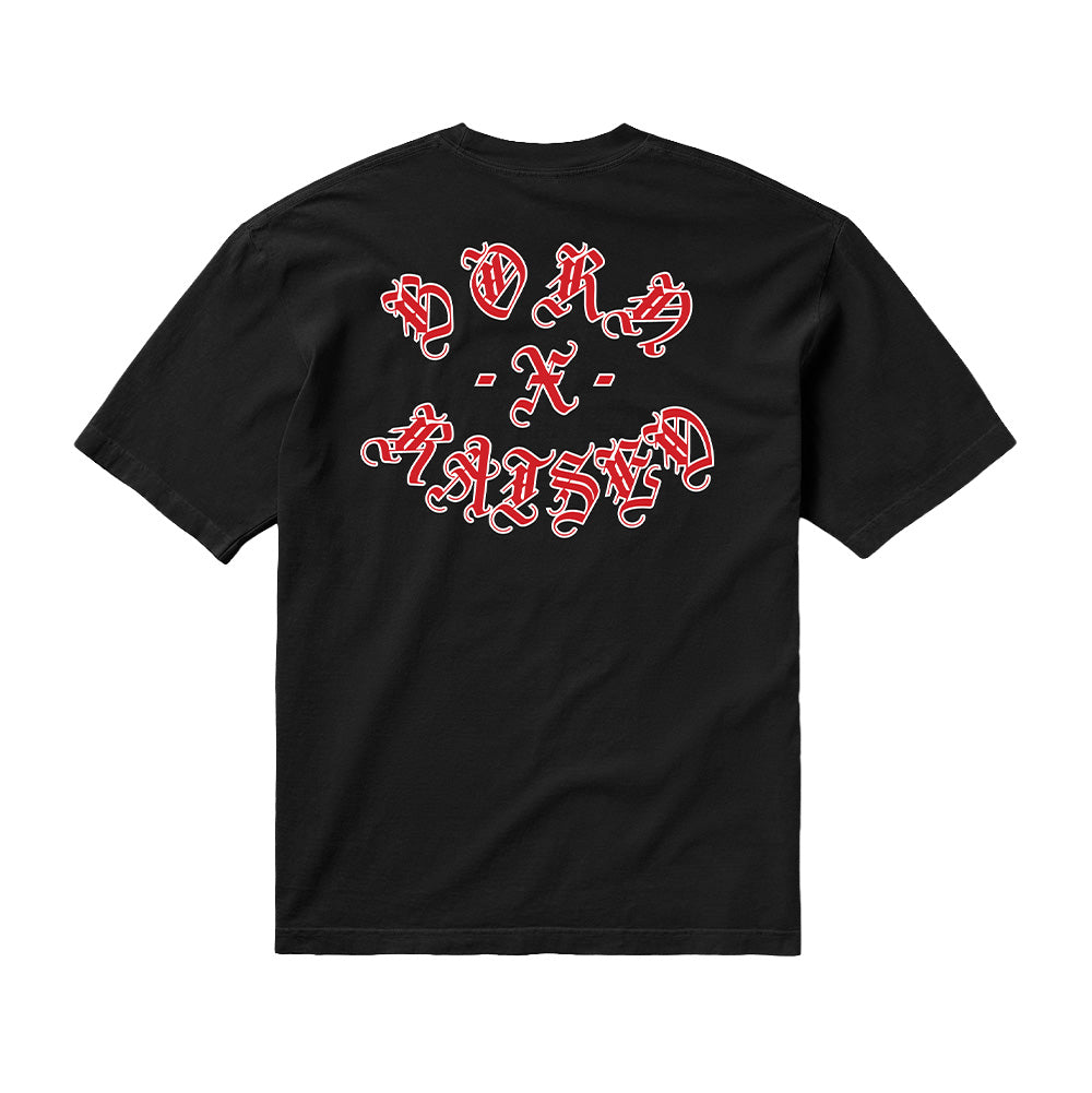 Back flat lay studio view of the Born X Raised Gothic Rocker T-Shirt in solid black, cut from heavy cotton jersey in a relaxed streetwear silhouette, centered by an oversized arched graphic print of the "BORN - X - RAISED" brand logo rendered in ornate red-and-white outlined Old English Gothic calligraphy across the upper back.