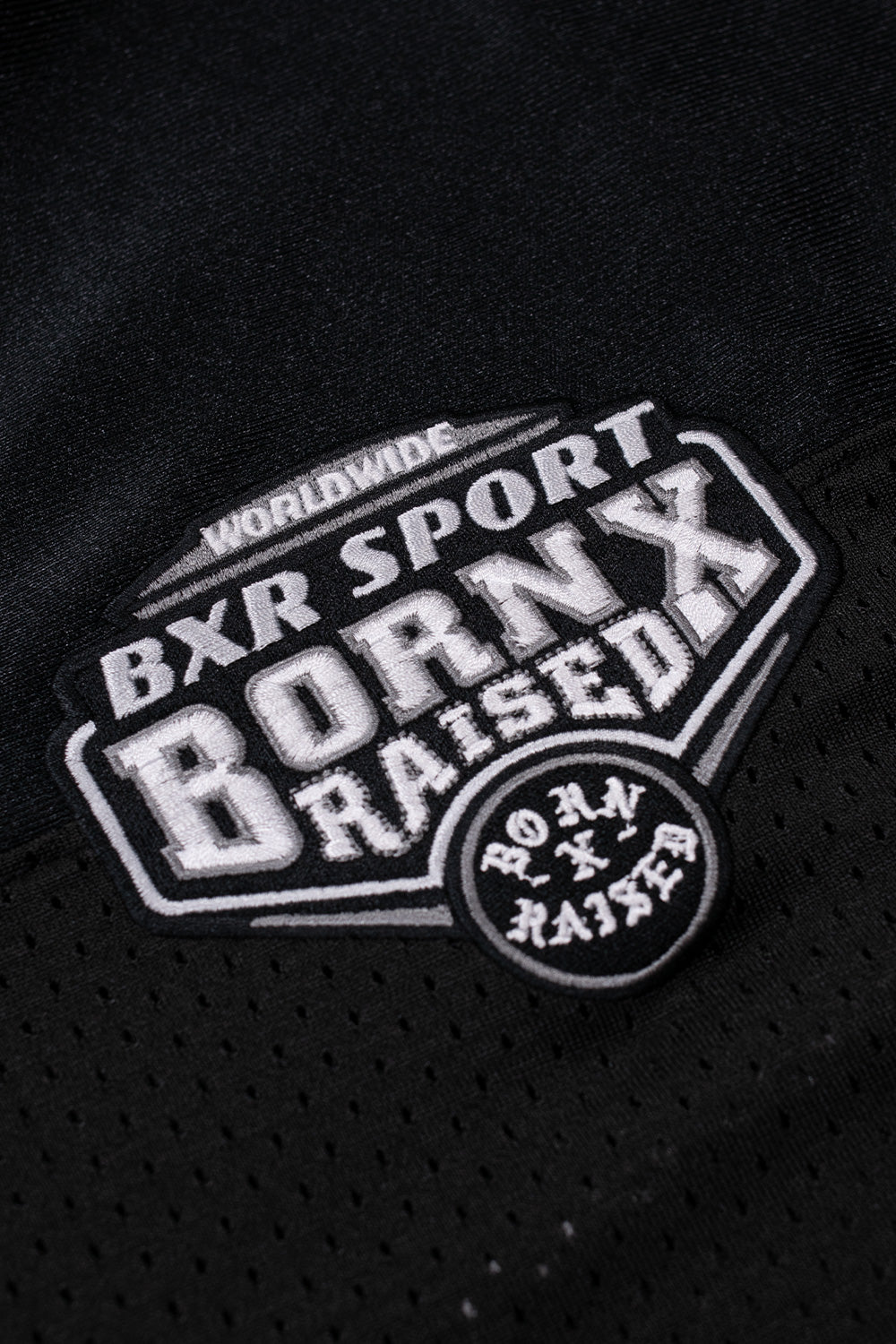 Close-up view of the embroidered BXR Sport Born X Raised crest logo patch on the chest of the black football jersey.