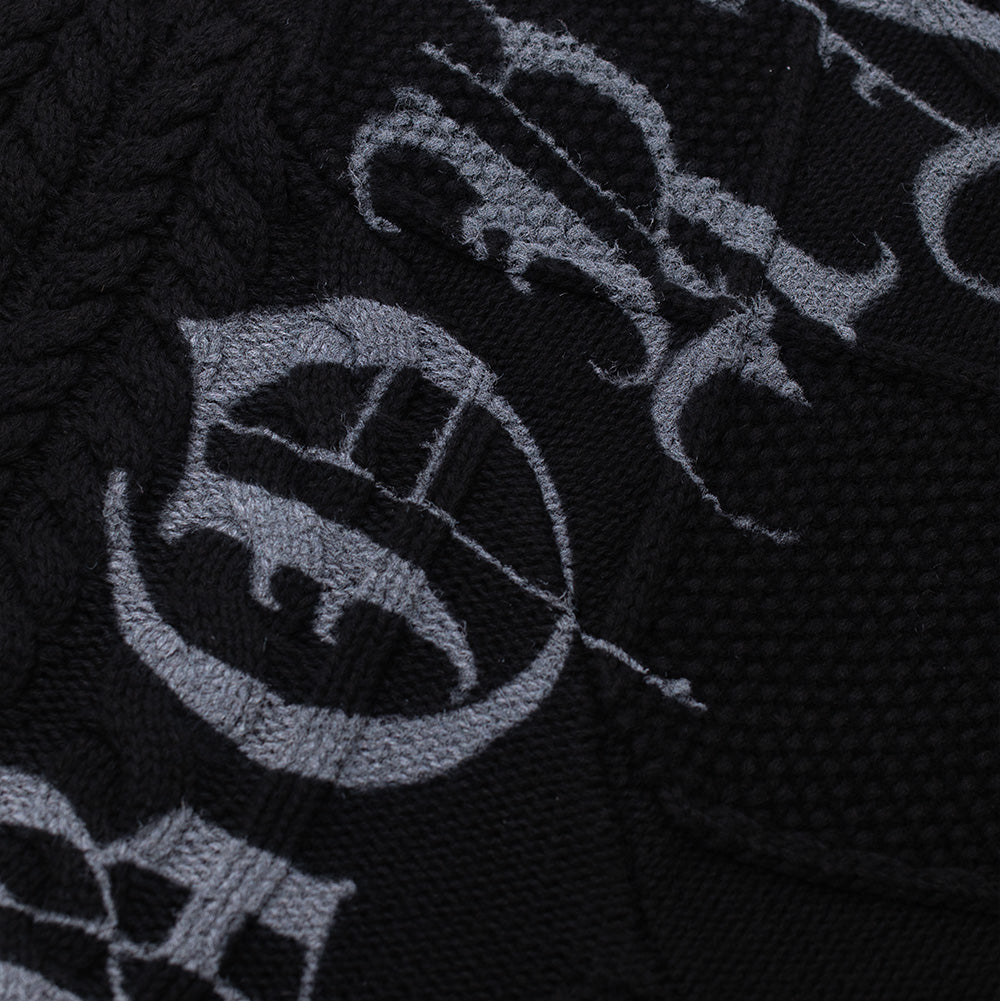 Macro studio view of the rear lettering on the black Born X Raised Cable Knit Sweater, showcasing the distressed grey ink of the ornate Old English Gothic font reading "BORN-X-RAISED" seamlessly screen-printed over the raised ridges of the thick cable knit knitwear.