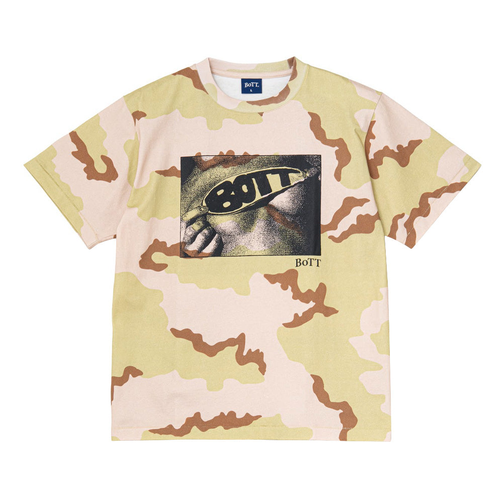Front flat lay studio view of the BoTT Lust T-Shirt in all-over desert camouflage, displaying a relaxed short-sleeve skate silhouette in shades of sand, khaki green, and light brown, ribbed round collar with blue inner BoTT neck tag, and a rectangular halftone screen print across the chest featuring a cropped face wearing sunglasses with bold "BOTT" typography.