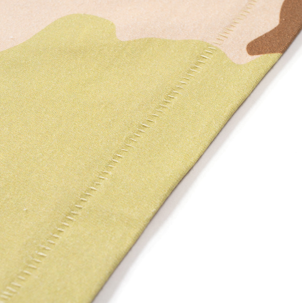 Macro studio close-up of the bottom hem on the BoTT Lust T-Shirt in Camo, highlighting the neat blind-stitch edge seam, finely woven cotton jersey texture, and organic curved borders of the printed desert camouflage pattern.