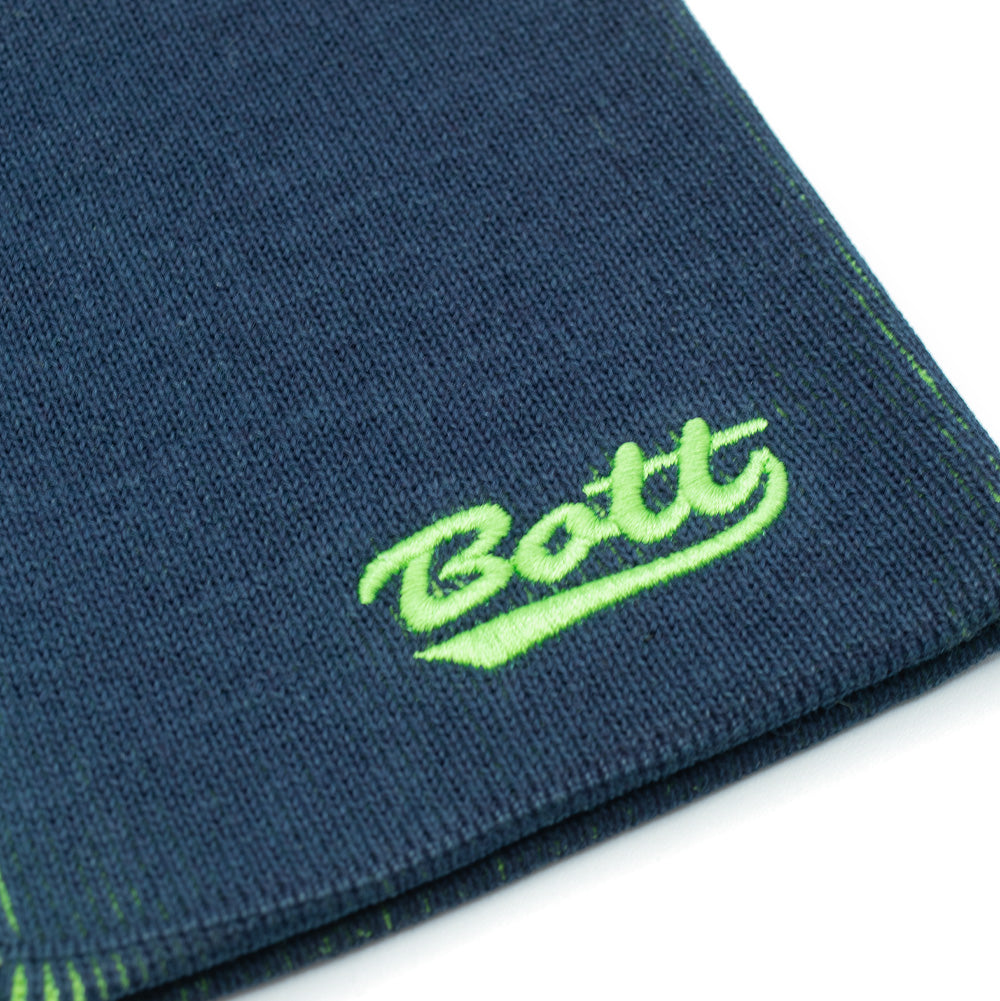 Macro studio close-up of the lower rim on the BoTT Overprint Skullcap Beanie in Navy, detailing the soft, elasticated knit fabric weave and high-density neon lime-green thread embroidery forming the underlined retro varsity-style cursive "BoTT" brand script.
