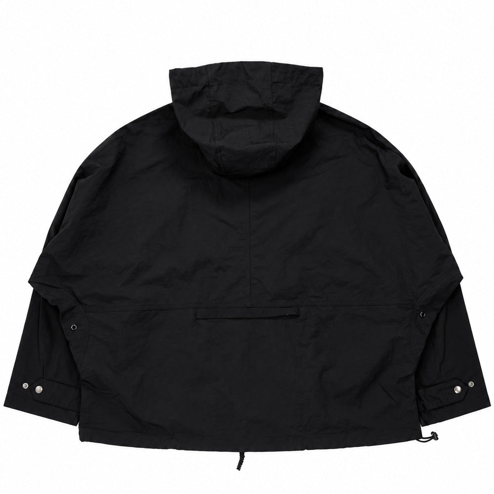 Back flat lay studio perspective of the black Brain Dead Dolman Sleeve Jacket, highlighting the voluminous, wide-cut cape silhouette created by the continuous dolman sleeve construction, structured multi-panel hood, horizontal zippered rear lumbar stash pocket with protective welt flap, and dual silver snap fasteners on the wrist cuffs.