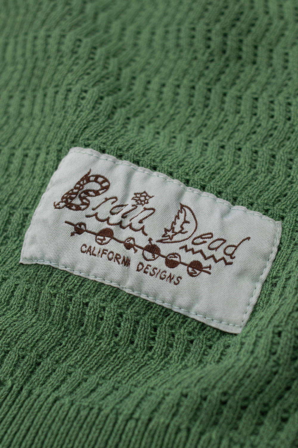 Brain Dead Pigment Dye Long Sleeve Polo Sweater Green logo patch – side logo label detail on knitted polo sweater made in Peru