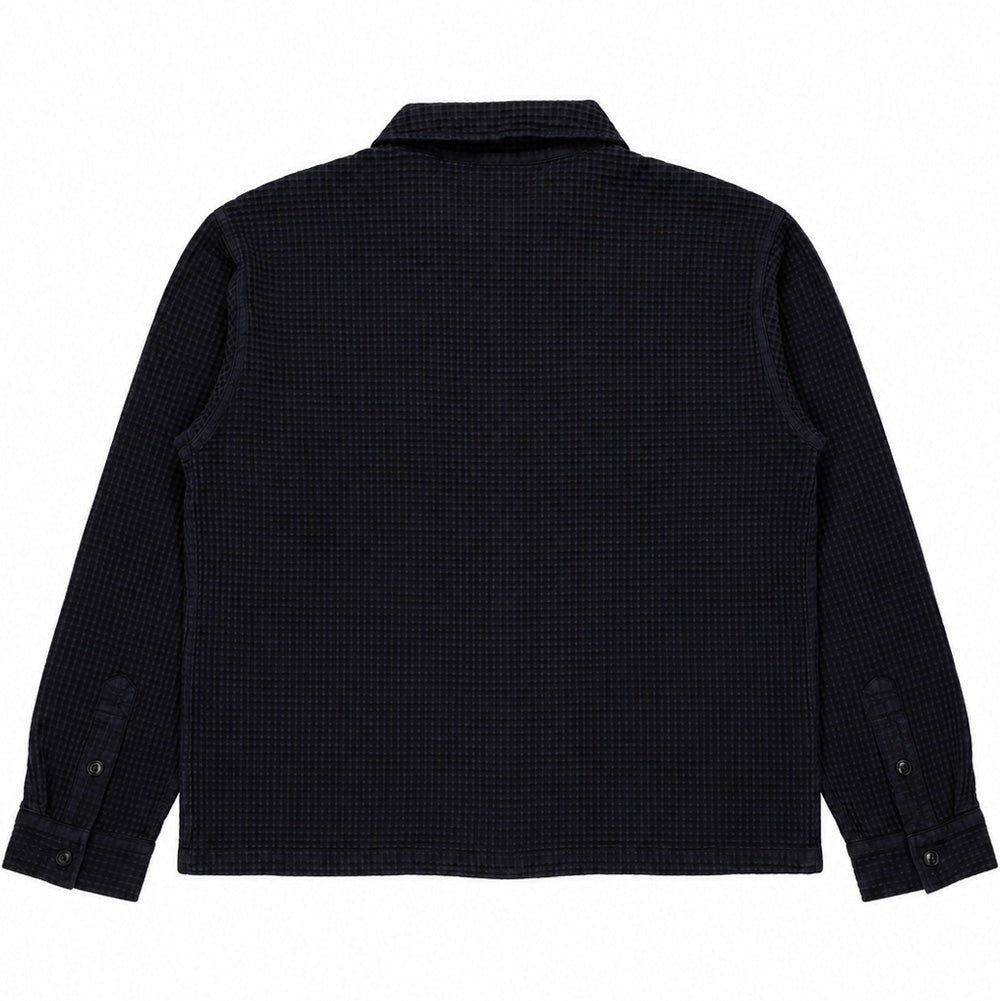 Back flat lay studio view of the black Brain Dead Waffle Button Front Shirt, displaying the seamless structured back panel, continuous textured waffle-knit cotton fabric drape, dropped shoulder seams, straight-cut waist hem, and button-cuffed long sleeves.