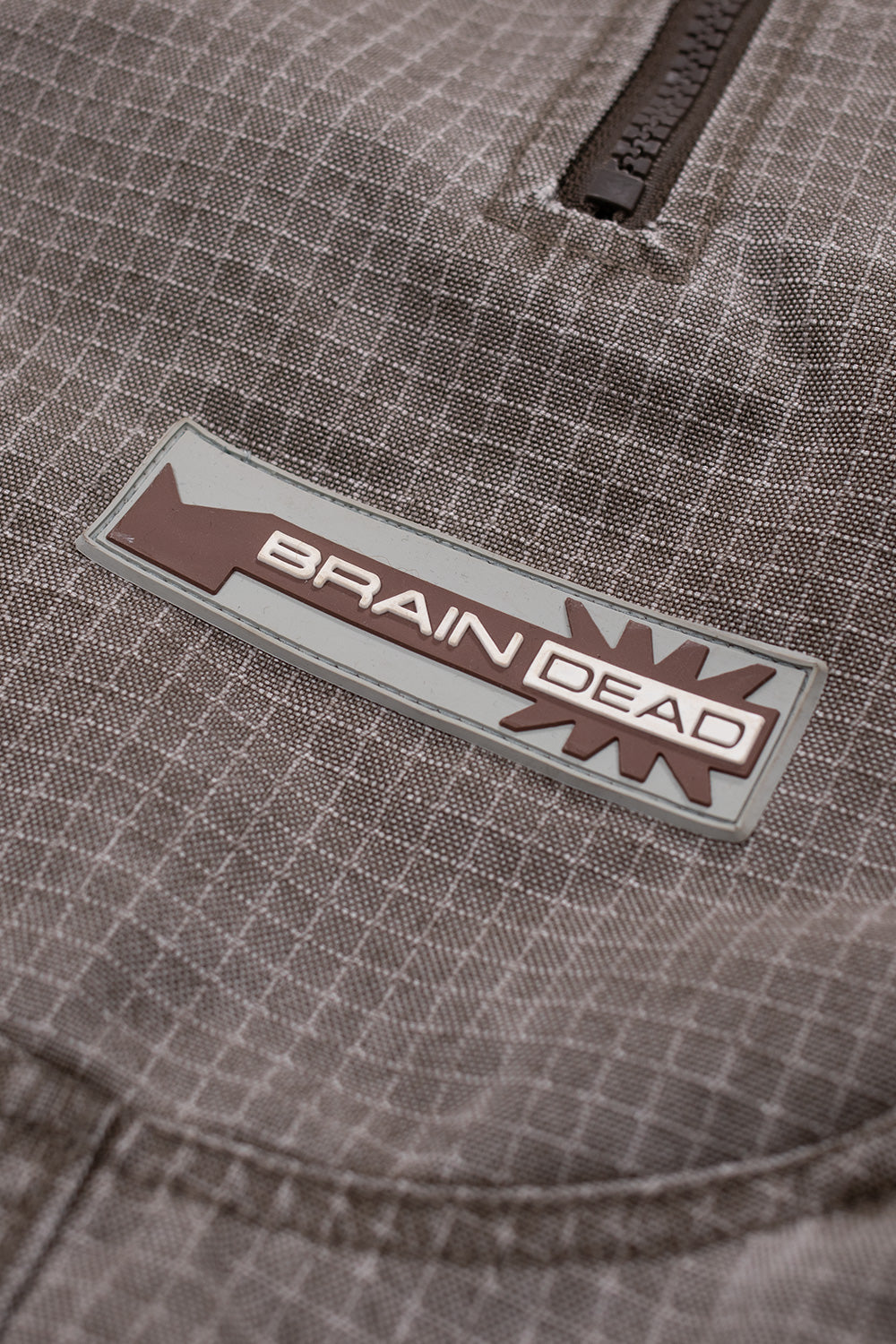 Brain Dead logo patch detail on Washed Ripstop Equipment Half Zip Brown pullover jacket highlighting branded rubber patch and grid ripstop weave material