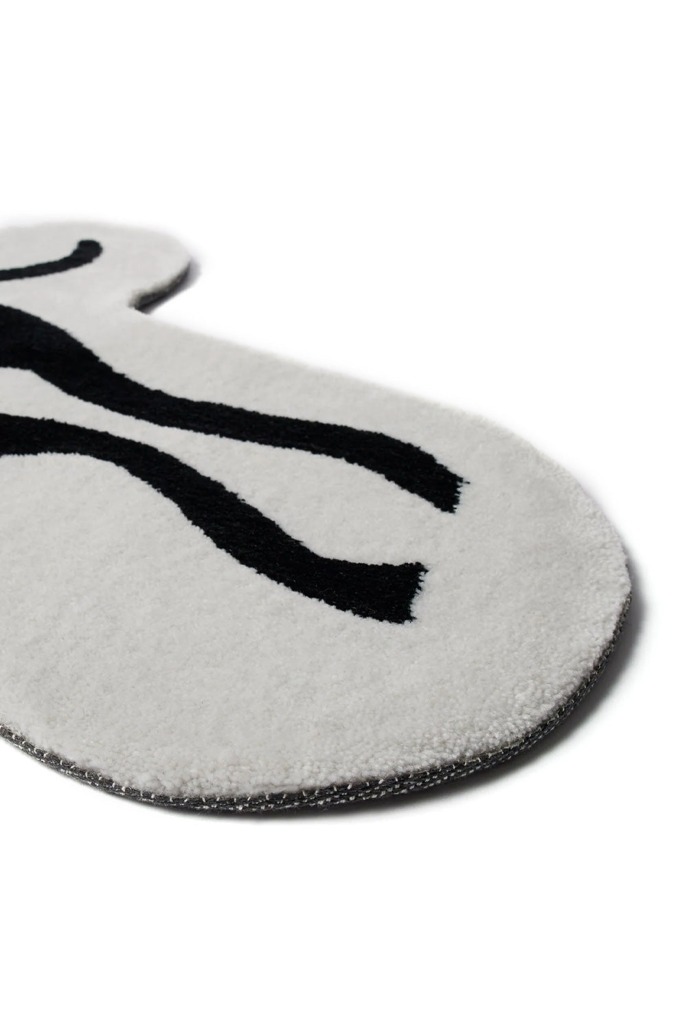 Angled low-perspective detail view of the edge of the By Parra High Heel Gloves Tufted Rug, showing the thick plush white tufted yarn pile, black graphic lines of the artwork, and curved reinforced border trim.