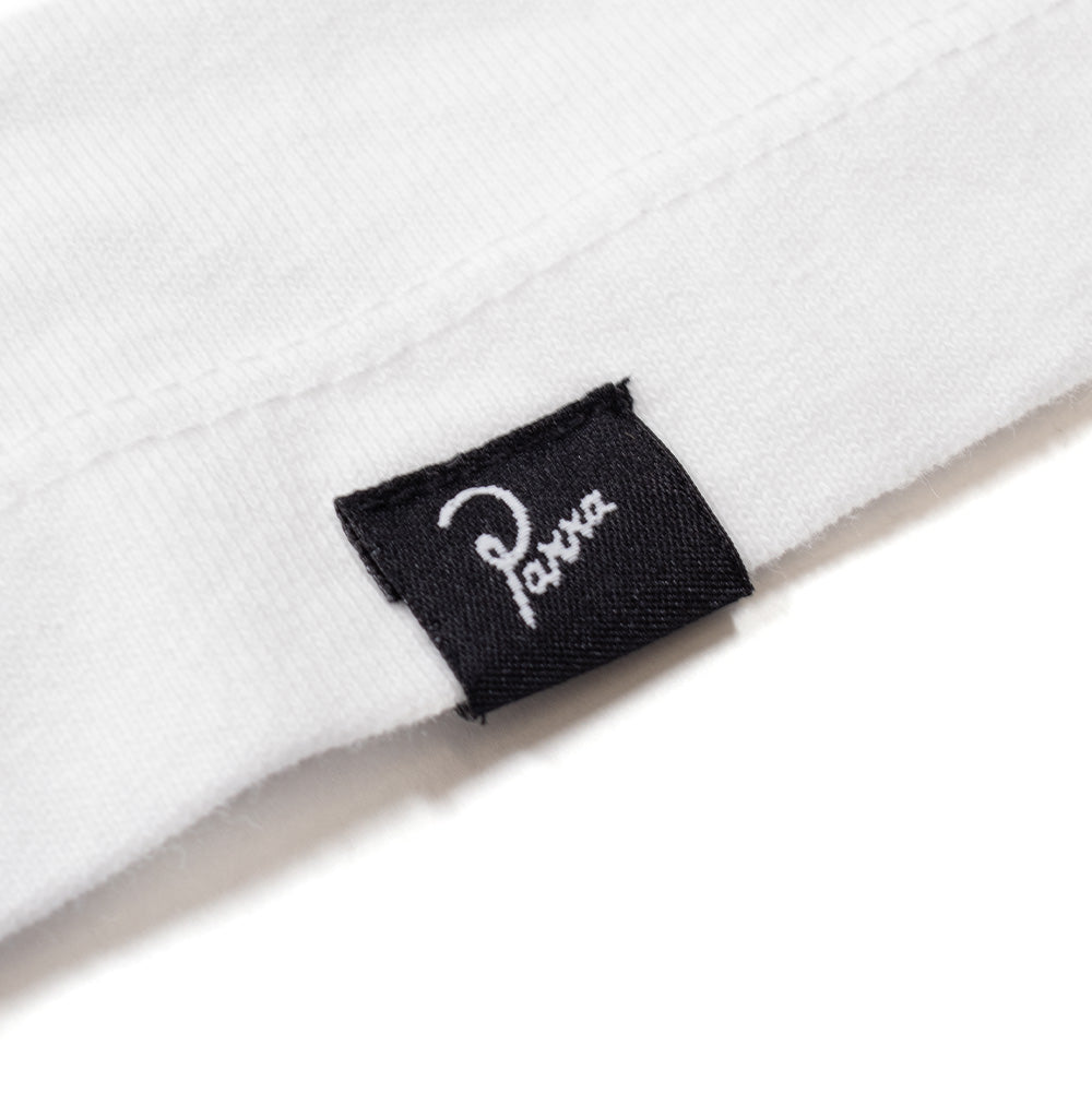 Extreme macro close-up of the lower left hem on the By Parra Not Listening T-Shirt, showcasing the clean parallel twin-needle stitch finishing and the small woven black brand flag label featuring white embroidered cursive "Parra" script.
