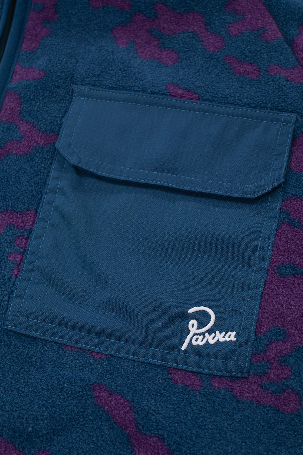 Close-up view of the left chest flap pocket on the By Parra Darwin Camo Fleece, showing the durable blue ripstop fabric with snap button closure and white stitched cursive Parra brand embroidery on the lower corner.