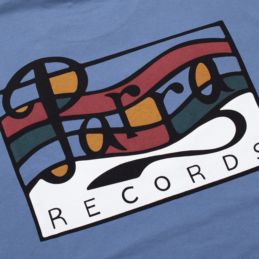 Detailed macro perspective of the back graphic on the By Parra Records T-Shirt, highlighting the bold black outlines, rich screen-printed ink blocks of red, deep teal, amber, and crisp white filling the stylized musical wave composition behind the flowing cursive "Parra" script.