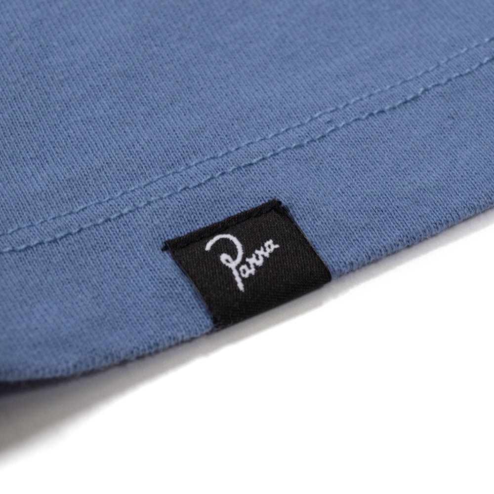Extreme macro close-up of the lower left hemline on the By Parra Records T-Shirt, detailing the double-needle edge stitching and a small woven black brand flag label featuring white embroidered cursive "Parra" script.