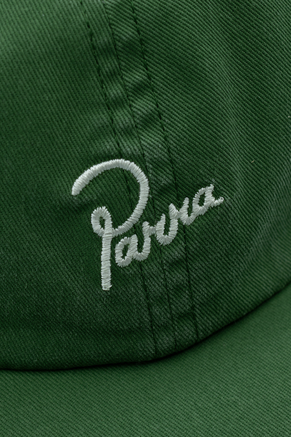 Extreme close-up macro detail of the white cursive Parra brand logo embroidery stitched on the heavy forest green pre-washed cotton twill fabric of the cap crown.