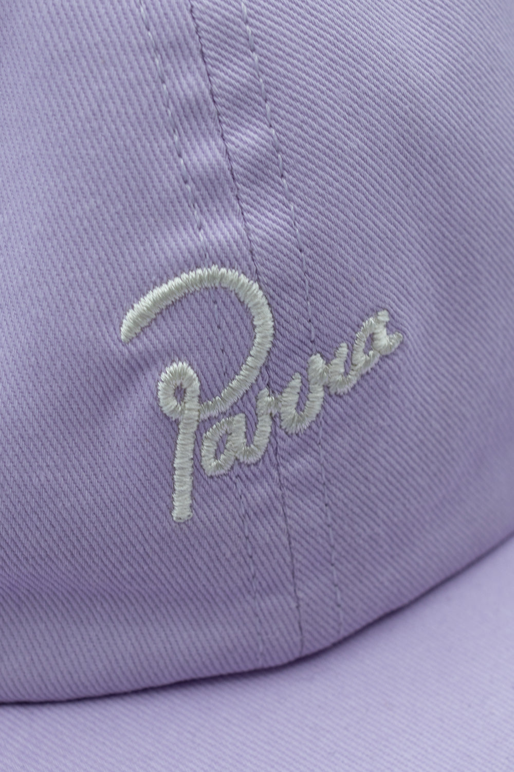 Extreme close-up detail shot of the white cursive Parra brand logo embroidery on the heavy lilac purple pre-washed cotton twill fabric of the cap crown.