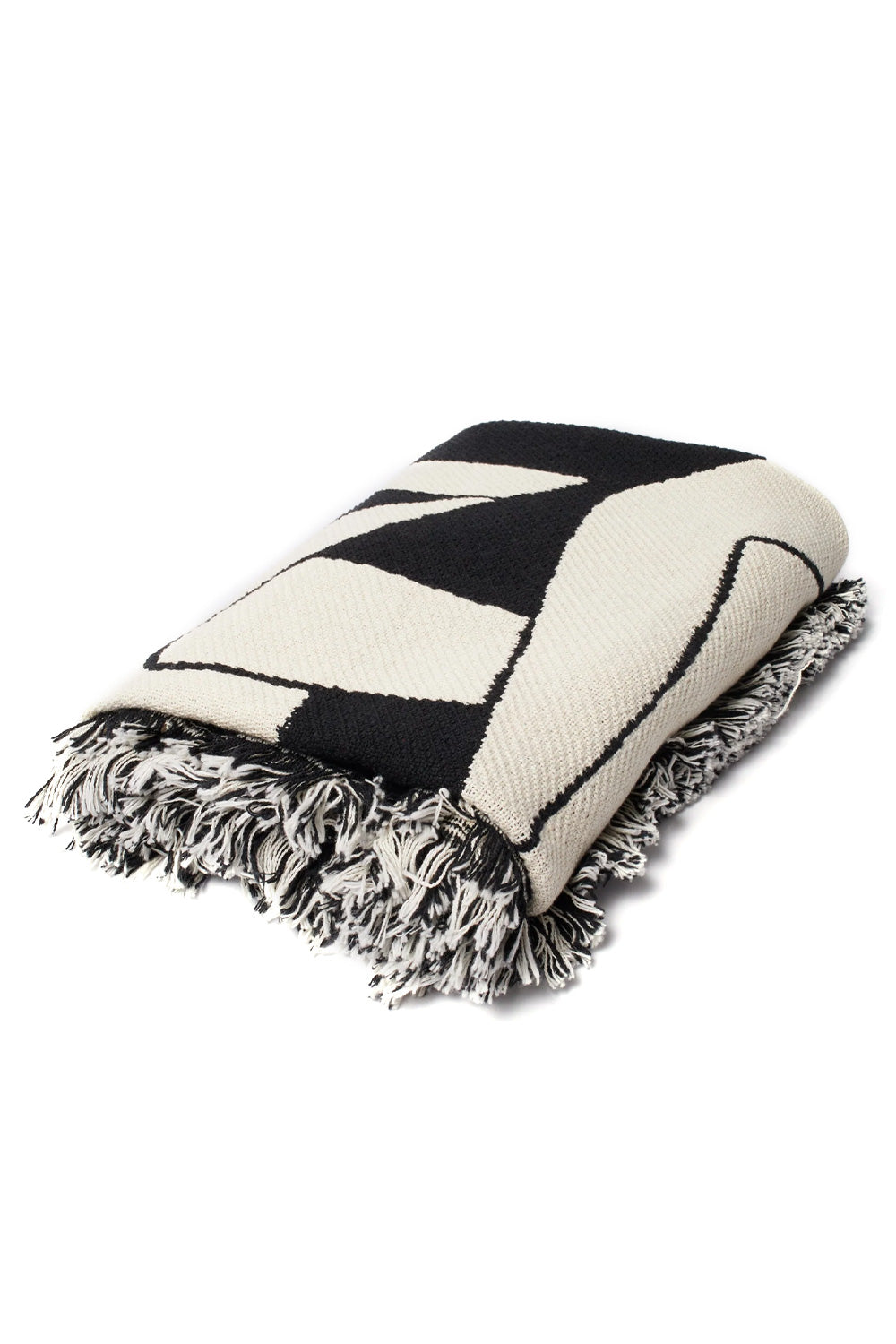 Studio shot of the folded By Parra Waiting For You cotton throw blanket, showcasing the plush layered textile folds, heavy-gauge jacquard knit structure, high-contrast monochrome pattern, and thick mixed black and white yarn tassel fringe.