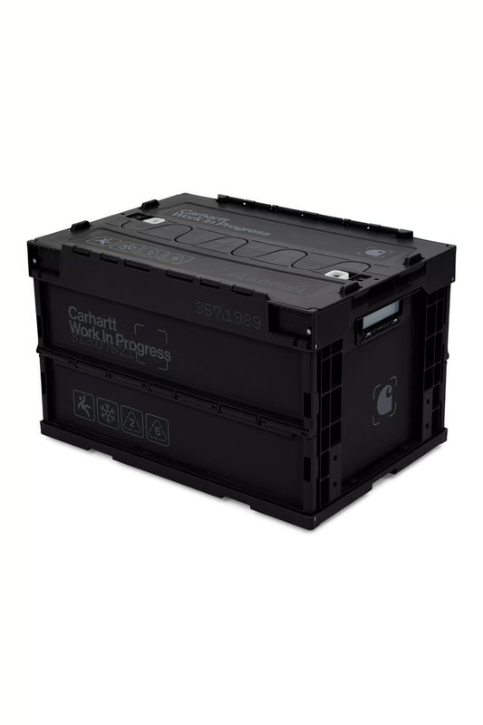 High-angle studio shot of the fully assembled Carhartt WIP Boxed Foldable Container in black and dark grey, featuring a 50-liter capacity, reinforced ribbed plastic frame, split-folding interlocked lid, side carry handles, printed Carhartt Work In Progress typography, and industrial icon graphics.