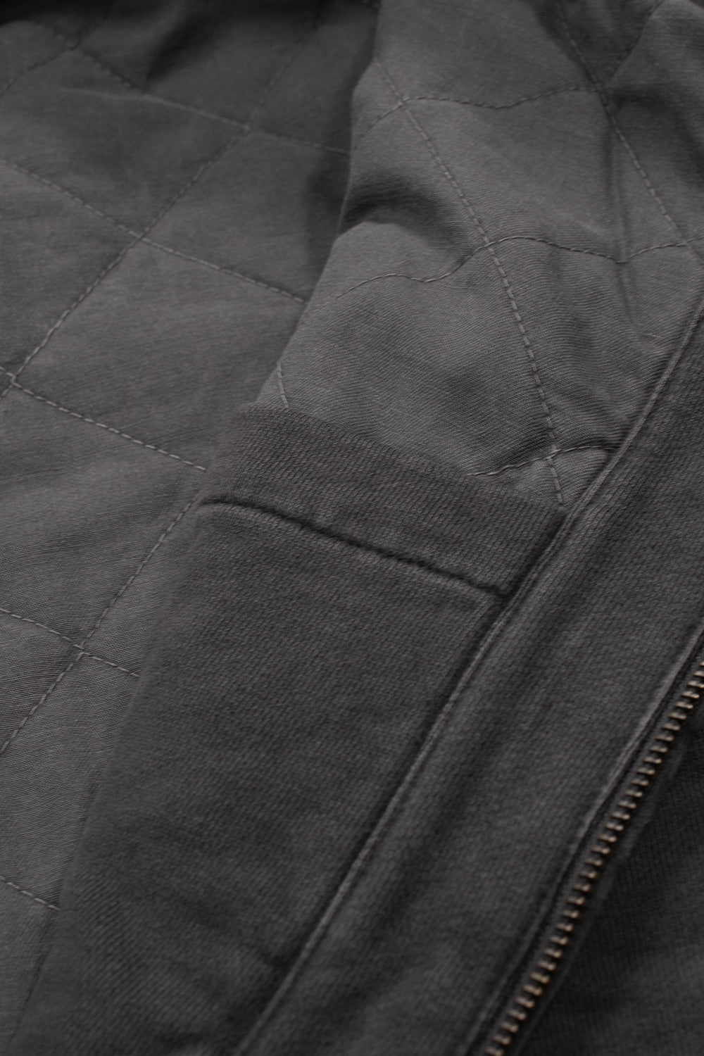 Interior macro perspective of the Carhartt WIP Hooded Vista Jacket, revealing the charcoal grey diamond-quilted insulated padded lining, interior pocket facing, and reinforced stitching along the front zipper placket.