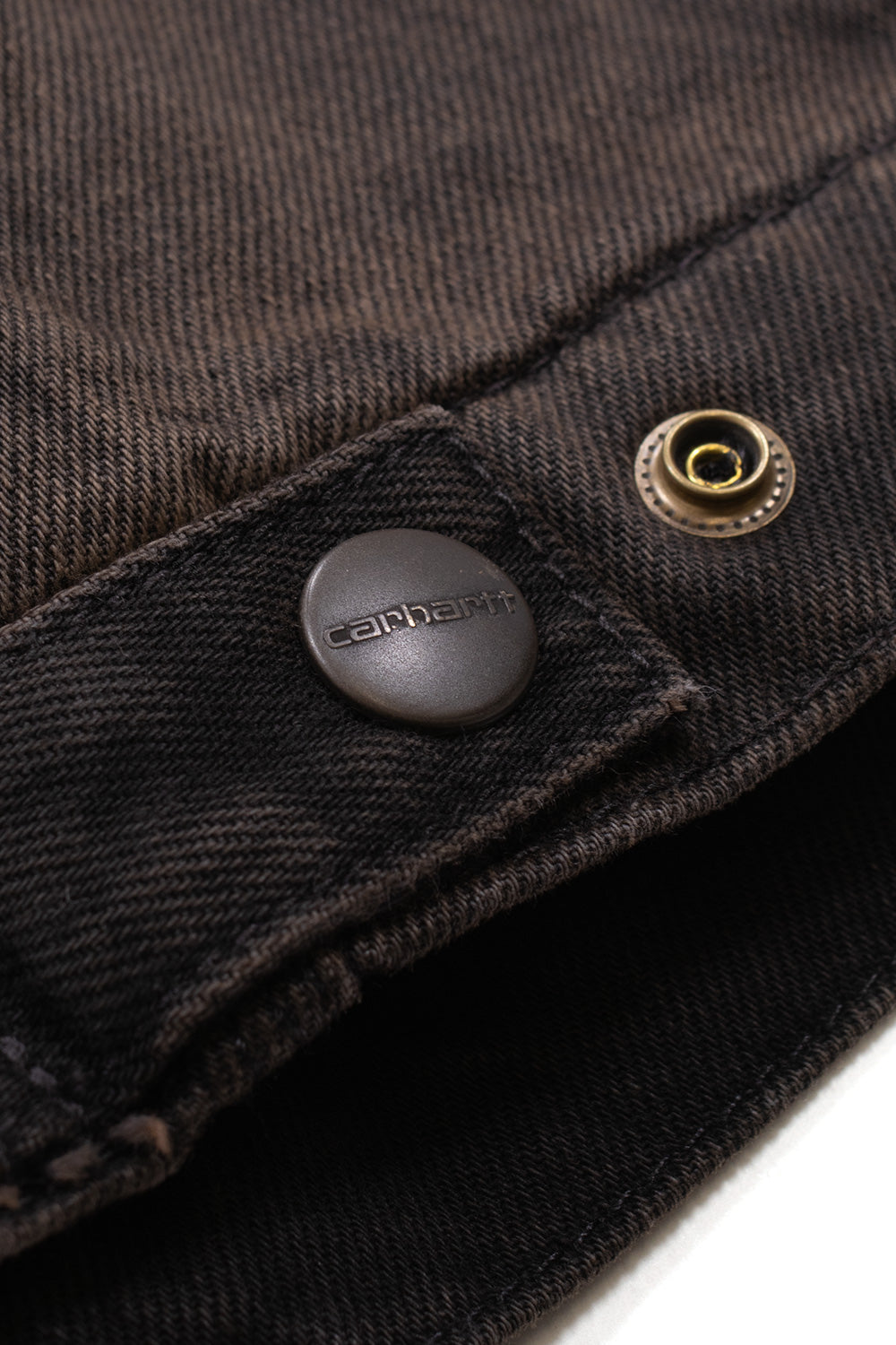 Macro studio shot of the adjustable sleeve cuff on the Carhartt WIP OG Detroit Jacket, focusing on the dark matte metal snap button debossed with the Carhartt wordmark and the heavy diagonal twill weave of the used-wash denim fabric.