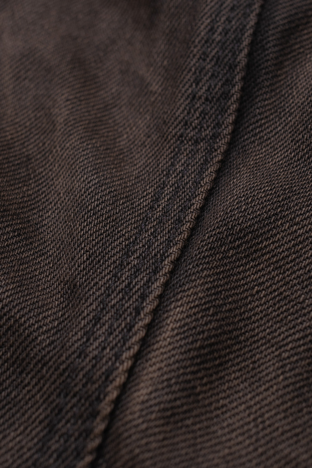 Extreme close-up texture shot of the denim twill on the Carhartt WIP OG Detroit Jacket, displaying the rich tobacco brown and black washed fade with sturdy tonal reinforced seam topstitching.