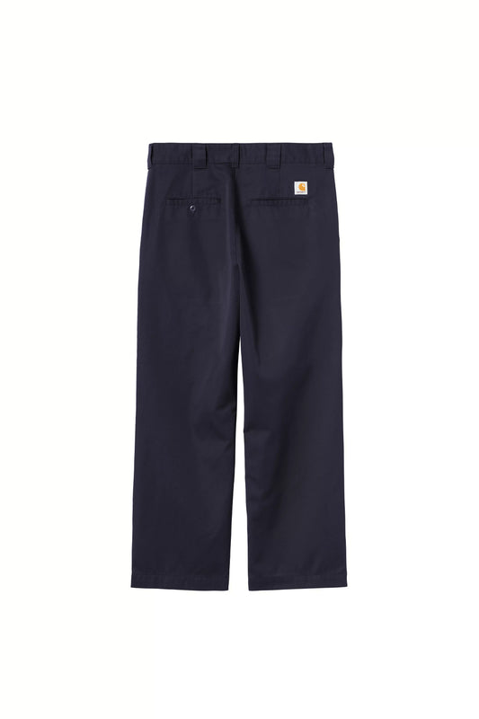 Rear flat lay view of the Carhartt WIP OG Master Pant in Dark Navy Rinsed, showcasing the loose straight-leg workwear fit in poly-cotton twill fabric, sturdy belt loops, two horizontal welt back pockets with button fastening on the left side, and the signature white and yellow square Carhartt woven logo patch on the right.