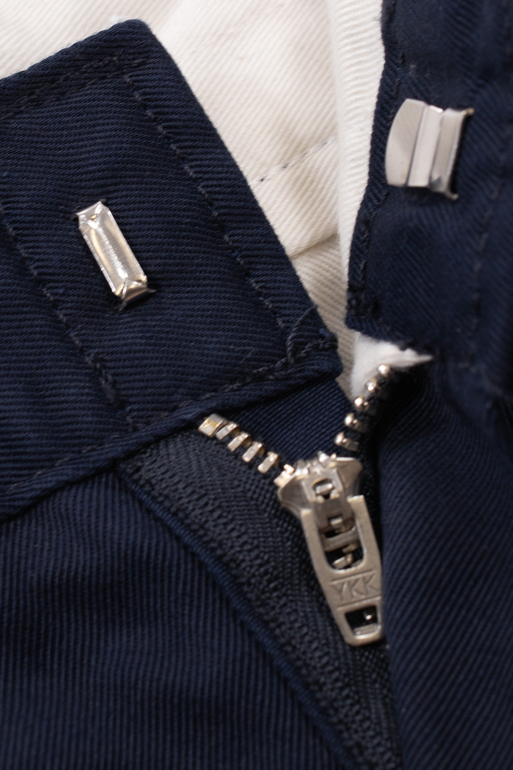 Detailed view of the front fly construction on the Carhartt WIP OG Master Pant in Dark Navy, displaying the concealed metal hook-and-bar waistband clasp, silver YKK metal zipper slider, and white interior waistband lining fabric.