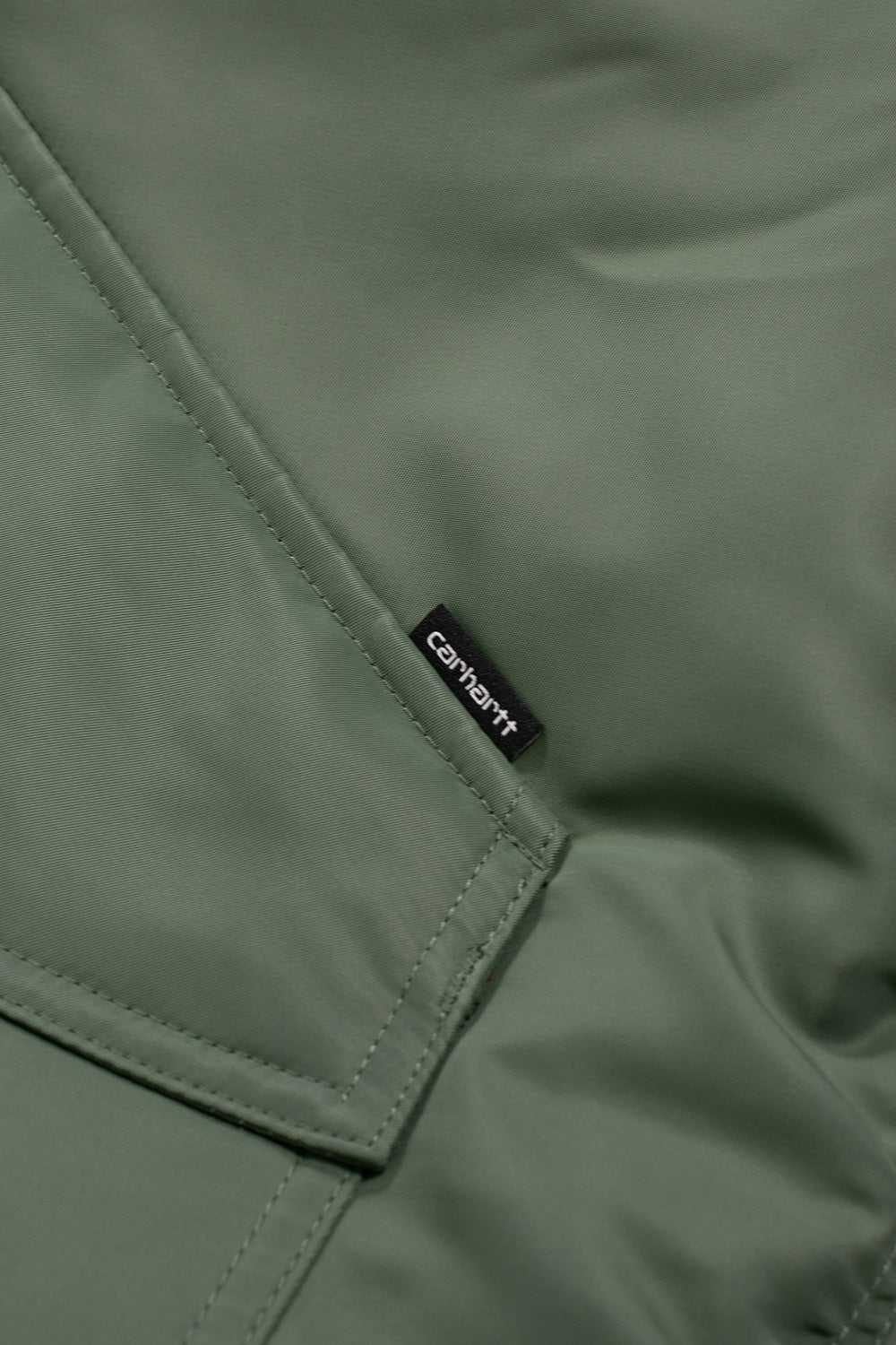 "Detailaufnahme der Carhartt WIP Olten Bomber Jacket in Duck Green/Turmeric – hochwertige Verarbeitung mit gewebtem Carhartt-Logo-Label"