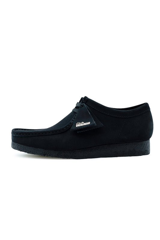Lateral side profile view of the Clarks Originals Wallabee shoe in Black Suede, displaying the deep black soft suede upper, traditional moccasin apron toe stitching, tonal black natural crepe rubber sole, and matching black suede fob tags.