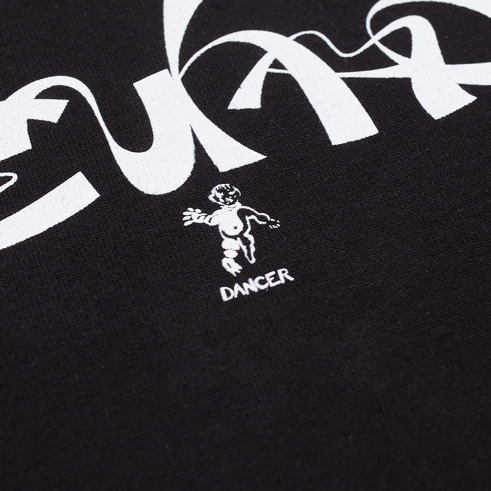 Detailed macro studio shot of the logo detail on the Dancer Copenhagen T-Shirt, highlighting the fine line screen print of the dancing cherub figurine above the clean "DANCER" brand lettering nestled beneath the flowing white curves of the calligraphic typography on deep black cotton jersey.