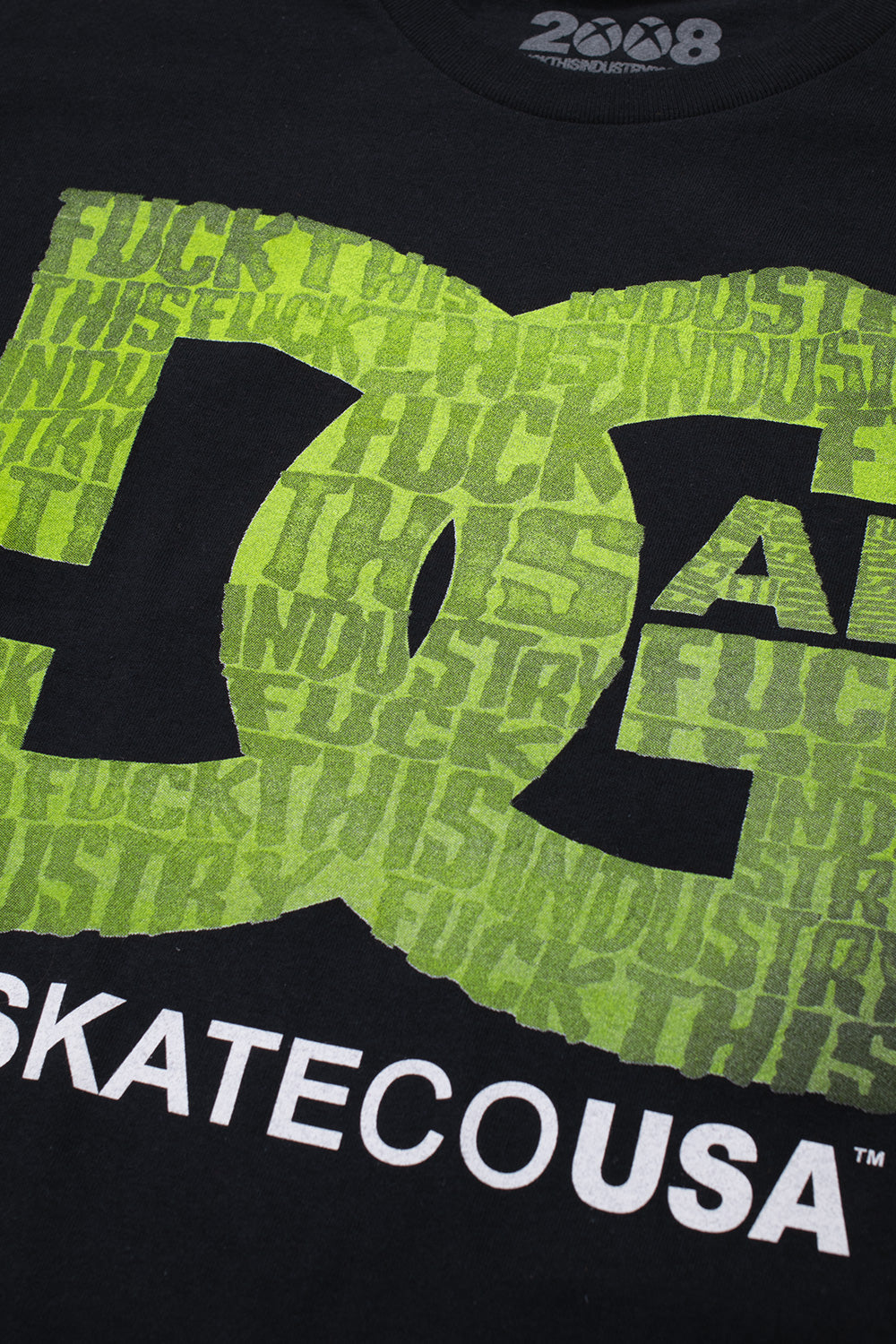 Close-up detailed view of the screen-printed chest graphic on the black Fuck This Industry DGAF T-Shirt, displaying the soft-touch neon green typography filling the stylized block letters, black interior collar print reading "2008 FUCKTHISINDUSTRY", and crisp white "SKATECOUSA" screen print across the black cotton jersey