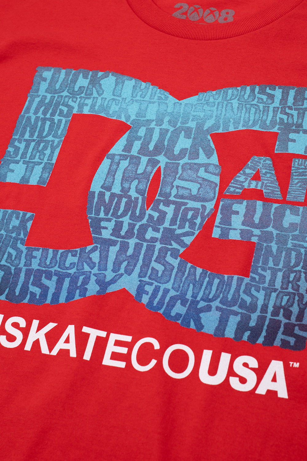 Close-up detailed view of the screen-printed graphic on the red Fuck This Industry DGAF T-Shirt, highlighting the textured red cotton jersey, the repetitive cyan and navy blue "FUCK THIS INDUSTRY" typography forming the iconic skate emblem, and the crisp white screen-printed "SKATECOUSA" lettering at the bottom