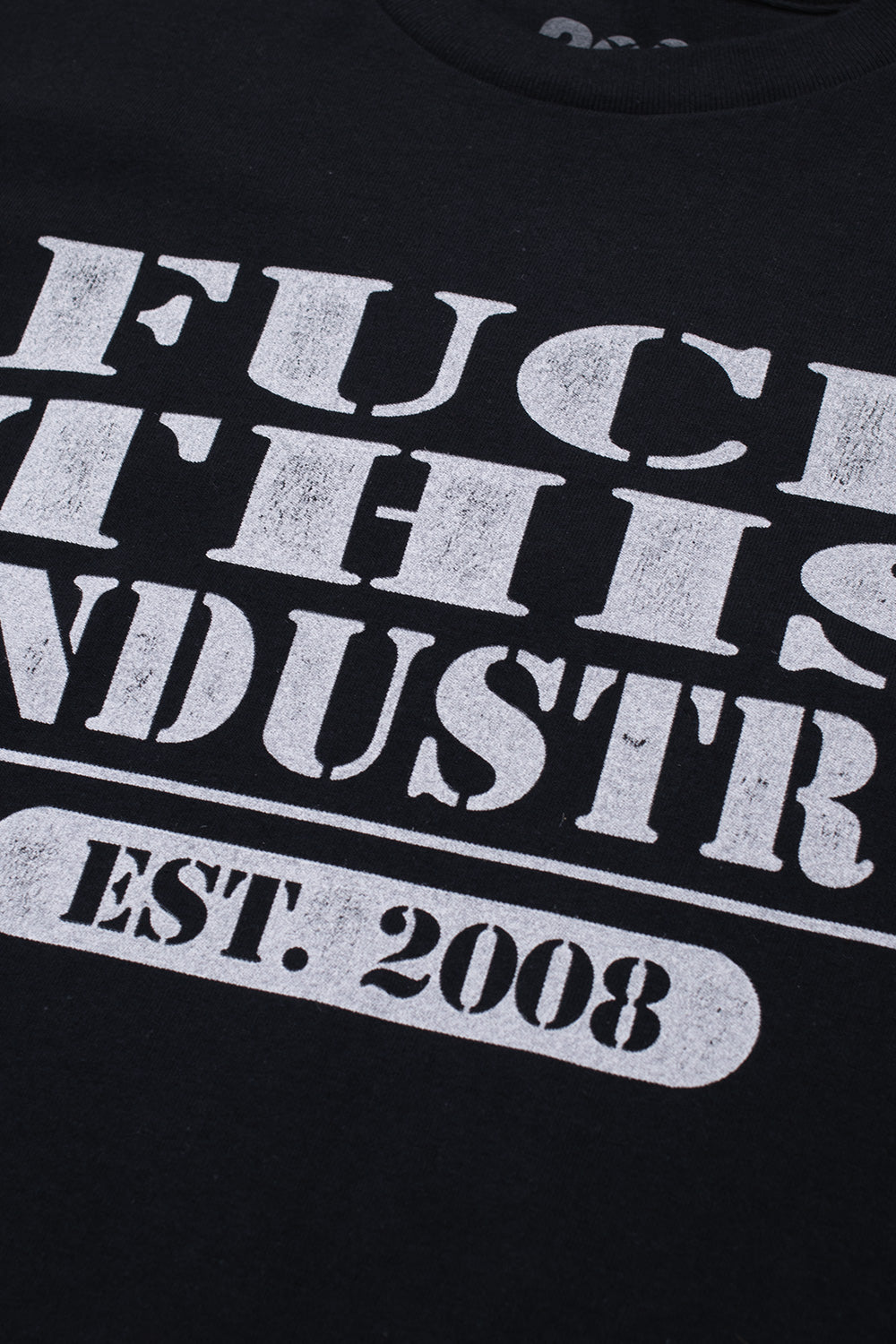 Macro close-up shot of the front chest graphic on the black Fuck This Industry T-Shirt, displaying the textured, cracked-ink vintage finish on the white "FUCK THIS INDUSTRY" serif block typography and the framed "EST. 2008" pill graphic