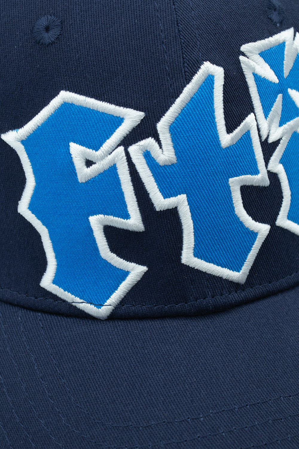 Macro close-up shot of the front embroidery on the navy Fuck This Industry Sorry Hat, highlighting the dimensional raised satin stitching of the royal blue and white "FT" lettering against the dense navy cotton fabric