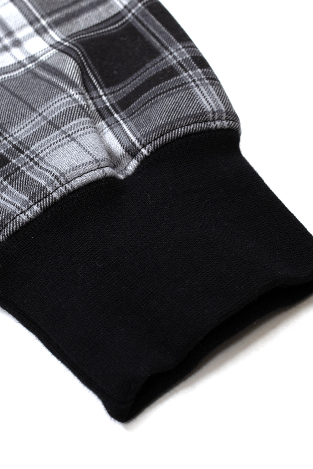 Macro detail shot of the sleeve cuff on the HUF Arch Plaid Full-Zip Hoodie, showing the seam joining the woven black, grey, and white tartan check cotton fleece body with the heavy elasticated solid black rib-knit wristband.