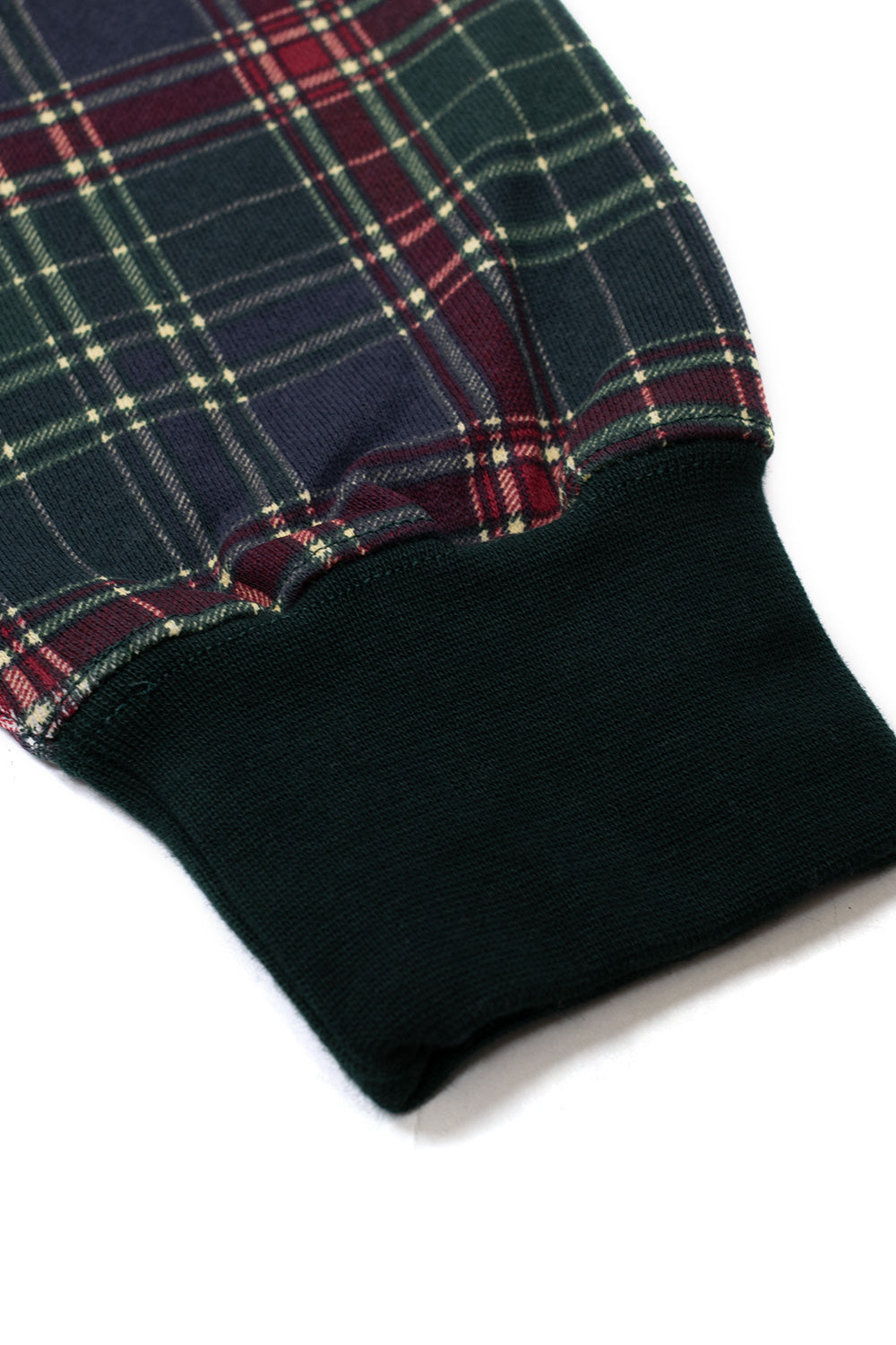 Macro detail shot of the sleeve cuff on the HUF Arch Plaid Full-Zip Hoodie, showing the transition between the durable woven green and red tartan check cotton fleece fabric and the thick elasticated dark forest green rib-knit wristband.
