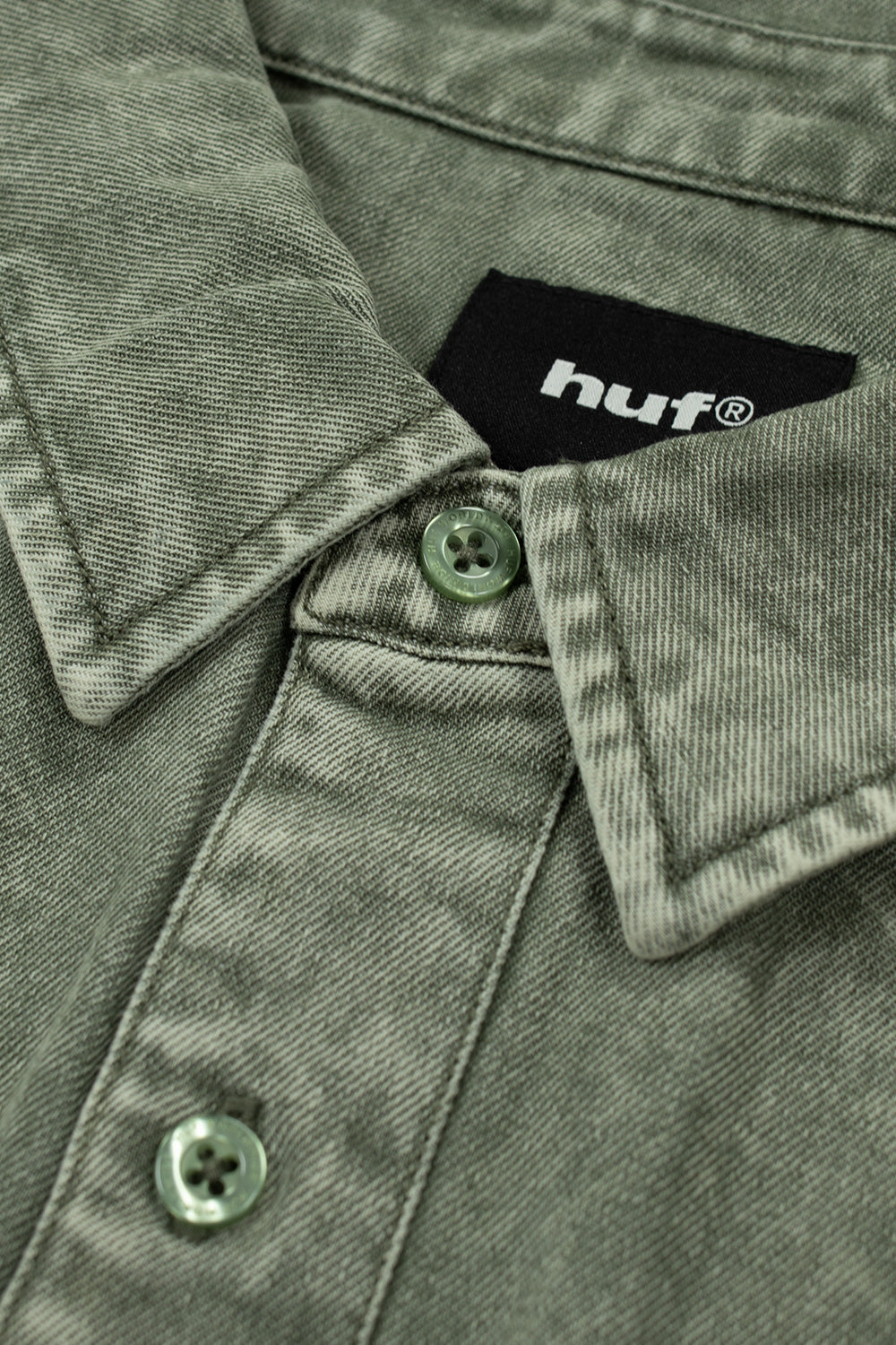 Detailed close-up shot of the point collar and upper front button placket on the olive HUF Carson Denim Shirt, highlighting the textured acid-washed cotton twill weave, tonal green buttons with debossed ring borders, and the interior black woven "HUF" neck label