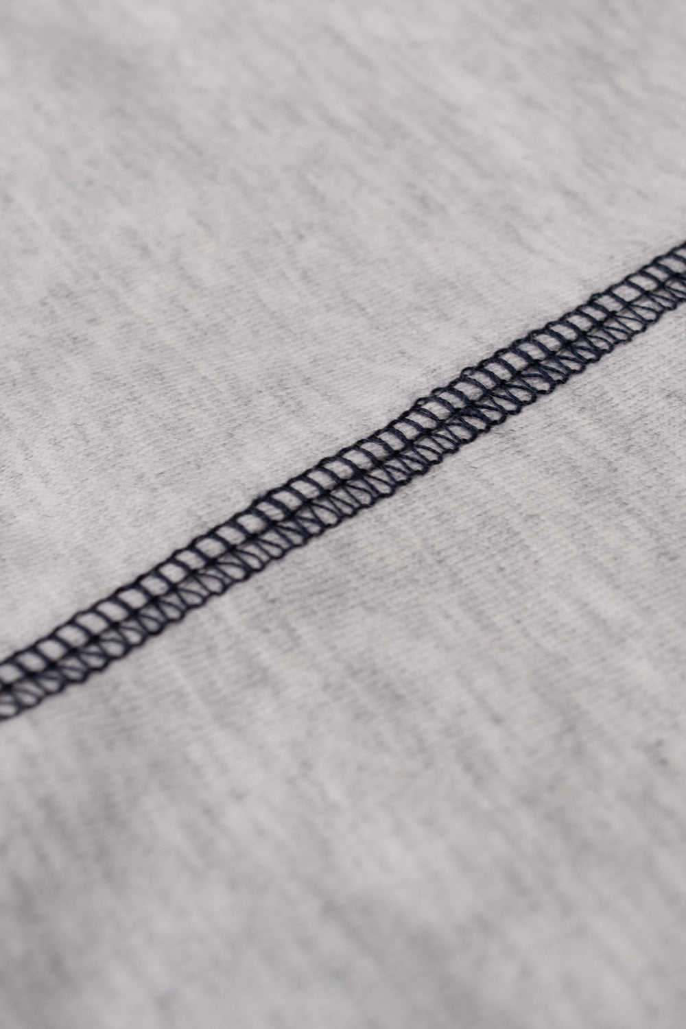 Extreme close-up detail of the durable dark navy contrast flatlock coverstitch seam running across the soft textured heather grey 240gsm cotton jersey fabric.